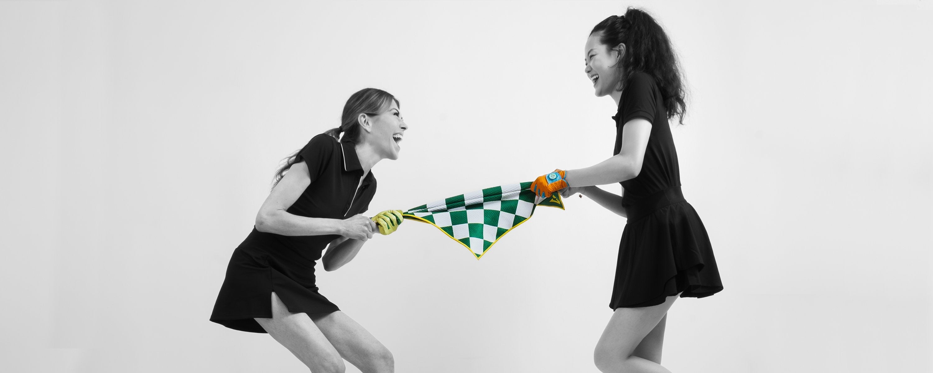 Two women playing tug of war with a magnetic golf towel in green and white checkers.