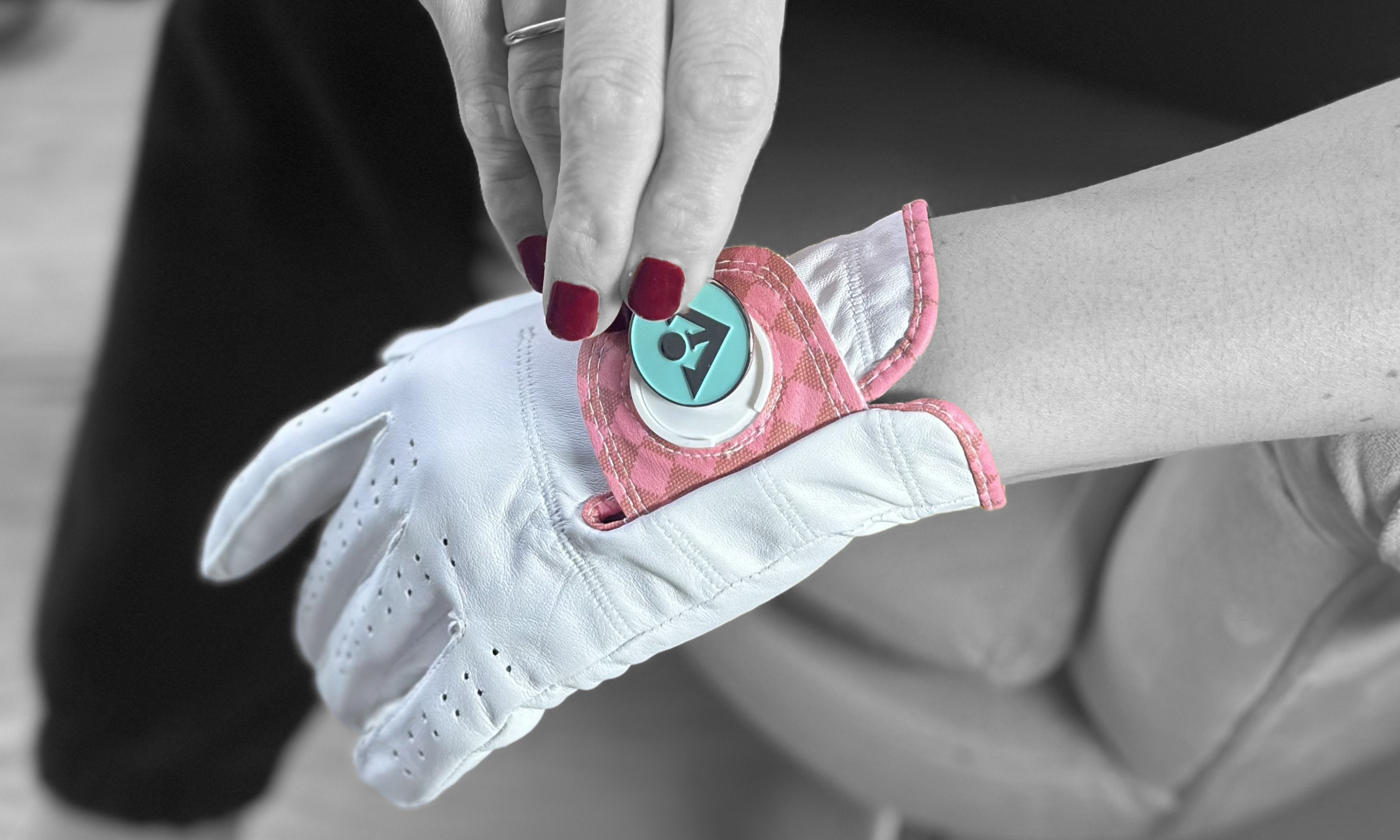 Various of our solid color ball markers with our logo on them scattered across a black and tile and white fixtures in the background, to compliment our magnetic golf gloves.
