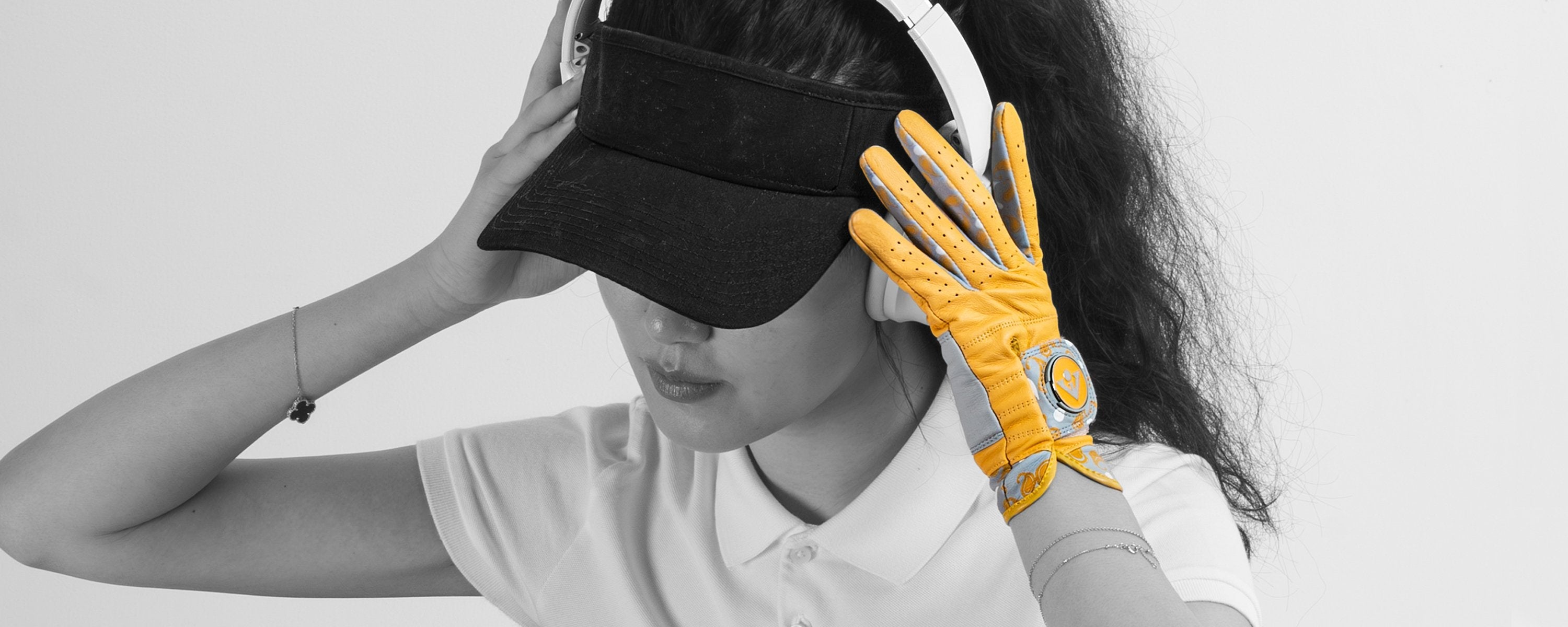Woman putting on her head phones in black and white while wearing a stylish womens golf glove in gold and grey.