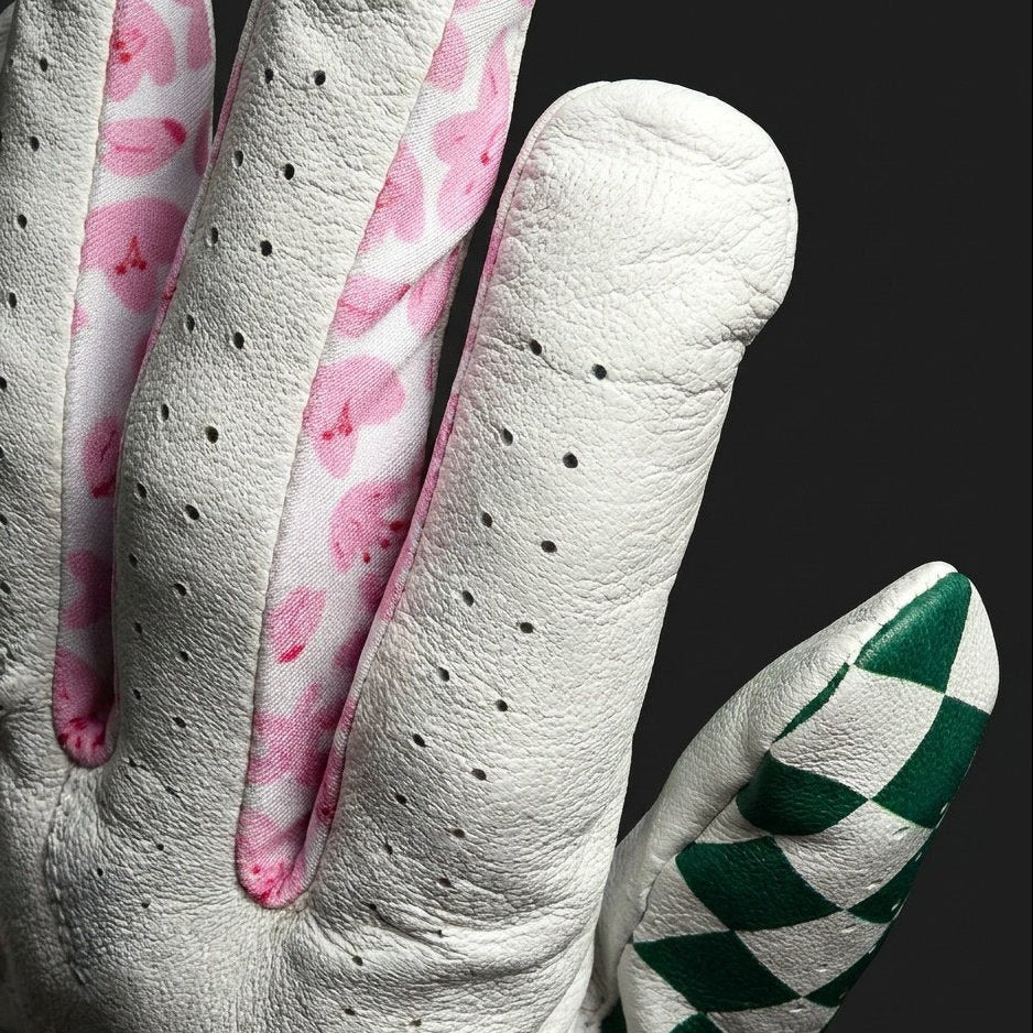 Close up of a golf glove with lycra between fingers in azaelas over a dark background.