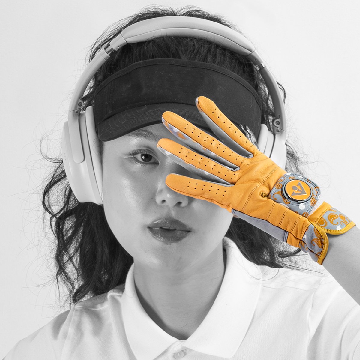 Women wearing a black visor and gold golf glove with magnetic ball marker posing it in front of her face in a black and white setting.