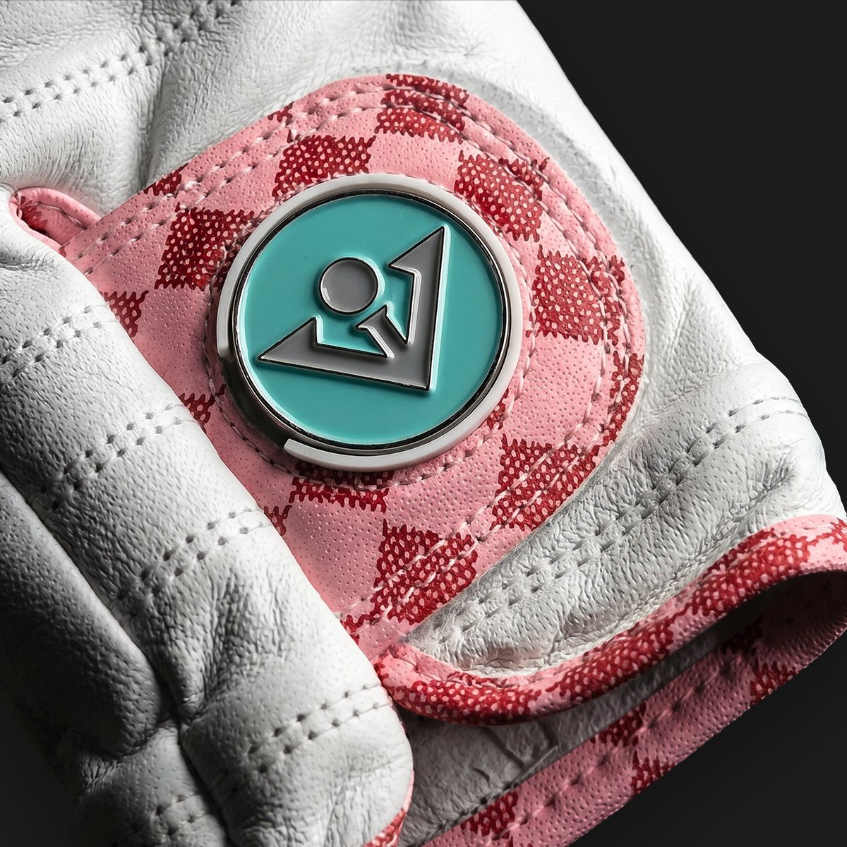 Close up of a golf glove with magnetic ball marker with pink stich and a blue ball marker.