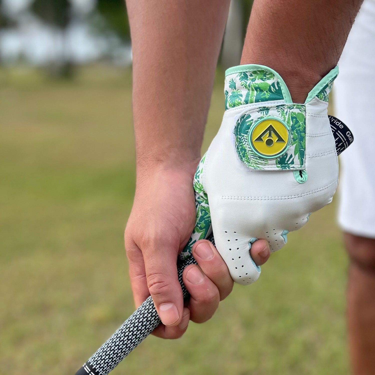 Golf glove with a tropical leaf pattern held by a person on a golf course.
