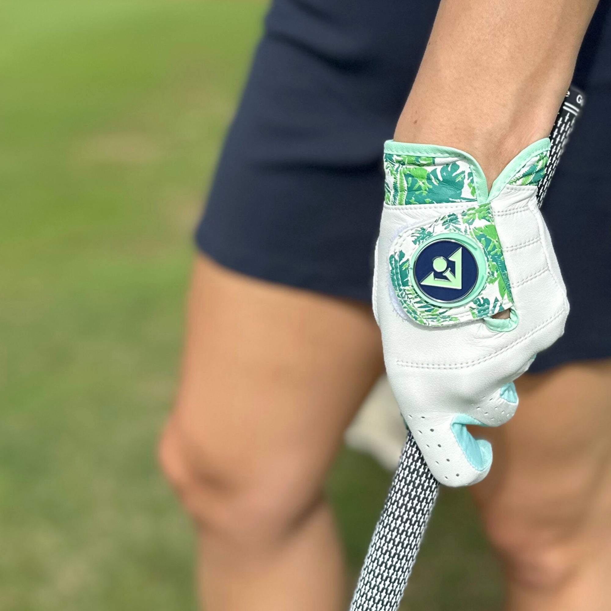 Woman in navy skirt holding a green floral golf glove with magnetic ball marker by VivanTee Golf.