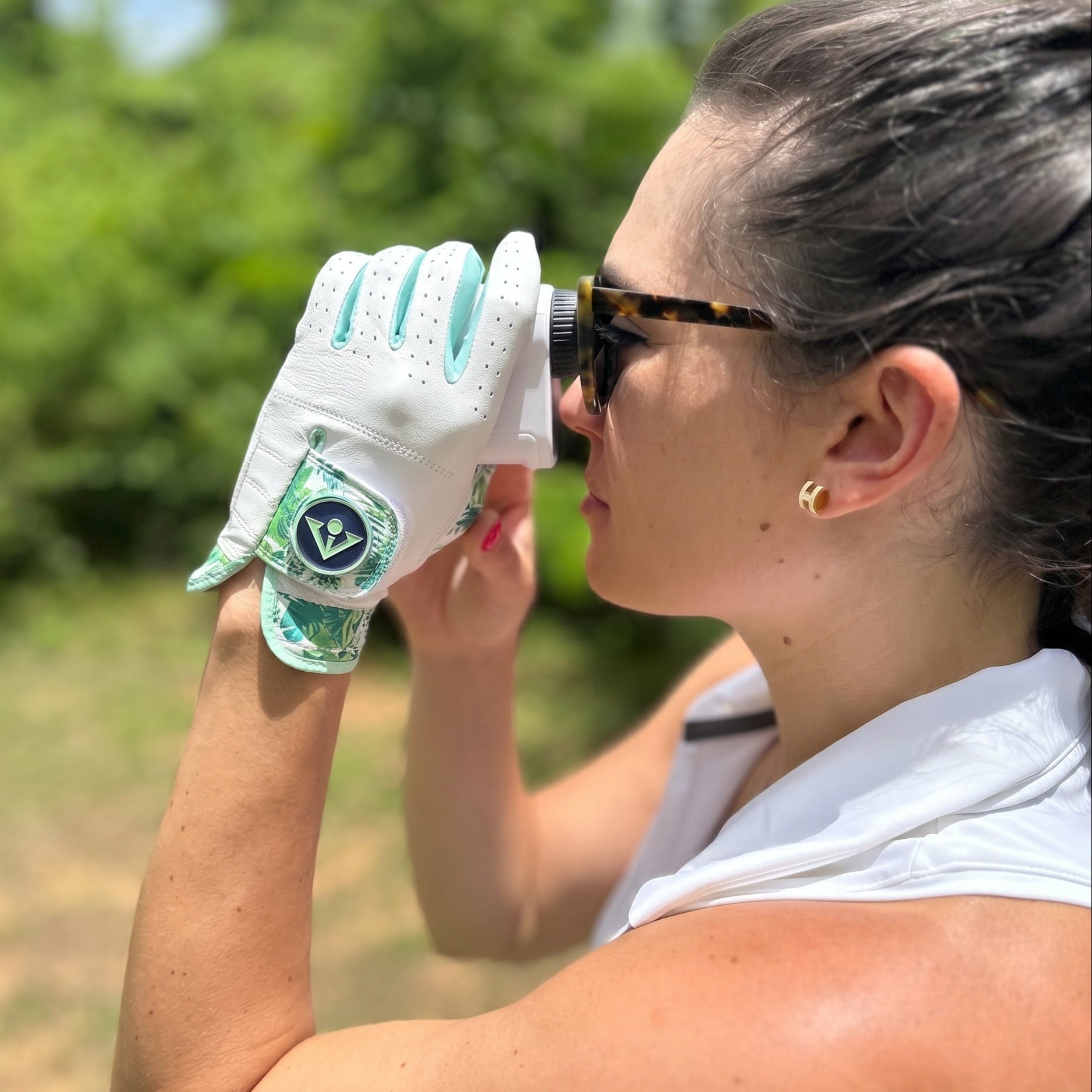 Woman golfer wearing a white tropical palm golf glove with a green VivanTee ball marker using a range finder outdoors.