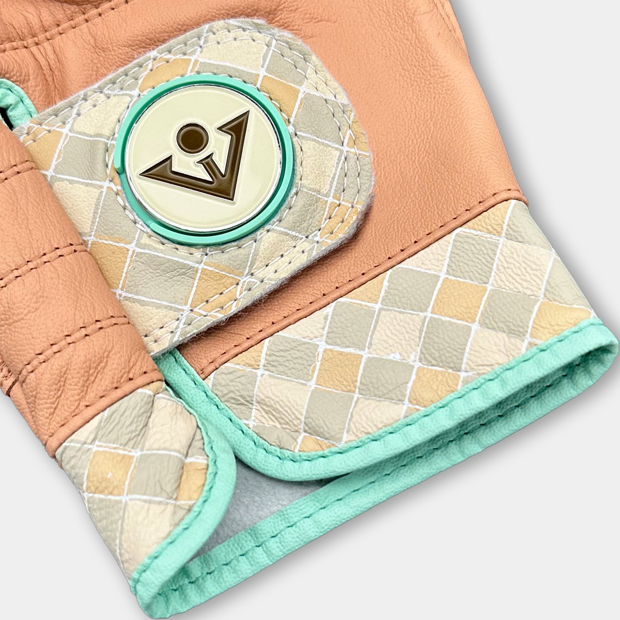 Close up of a tan and checkered golf glove with magnetic ball marker over a light grey background.