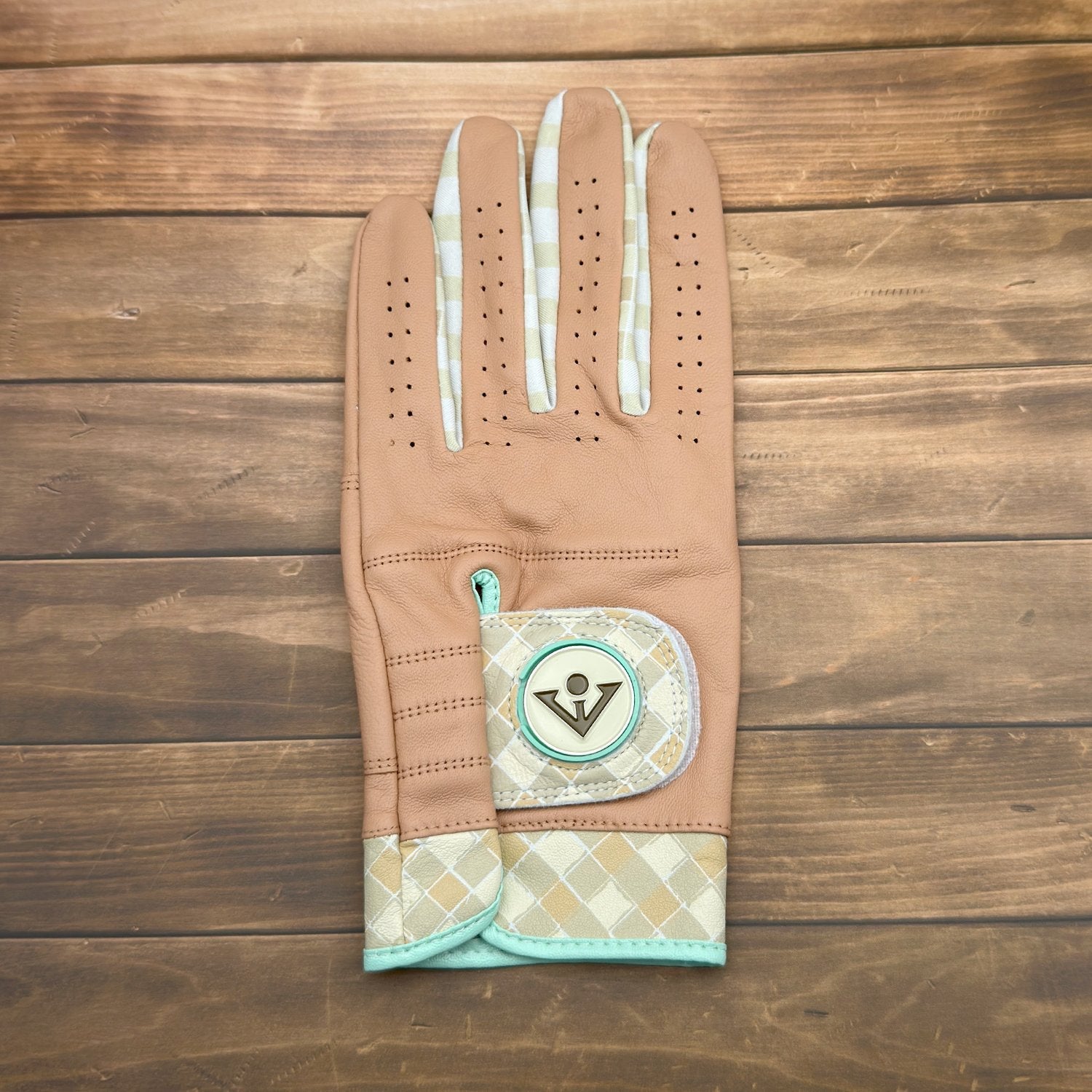 Brown and tan golf glove with ball marker laid out on a wooden deck.