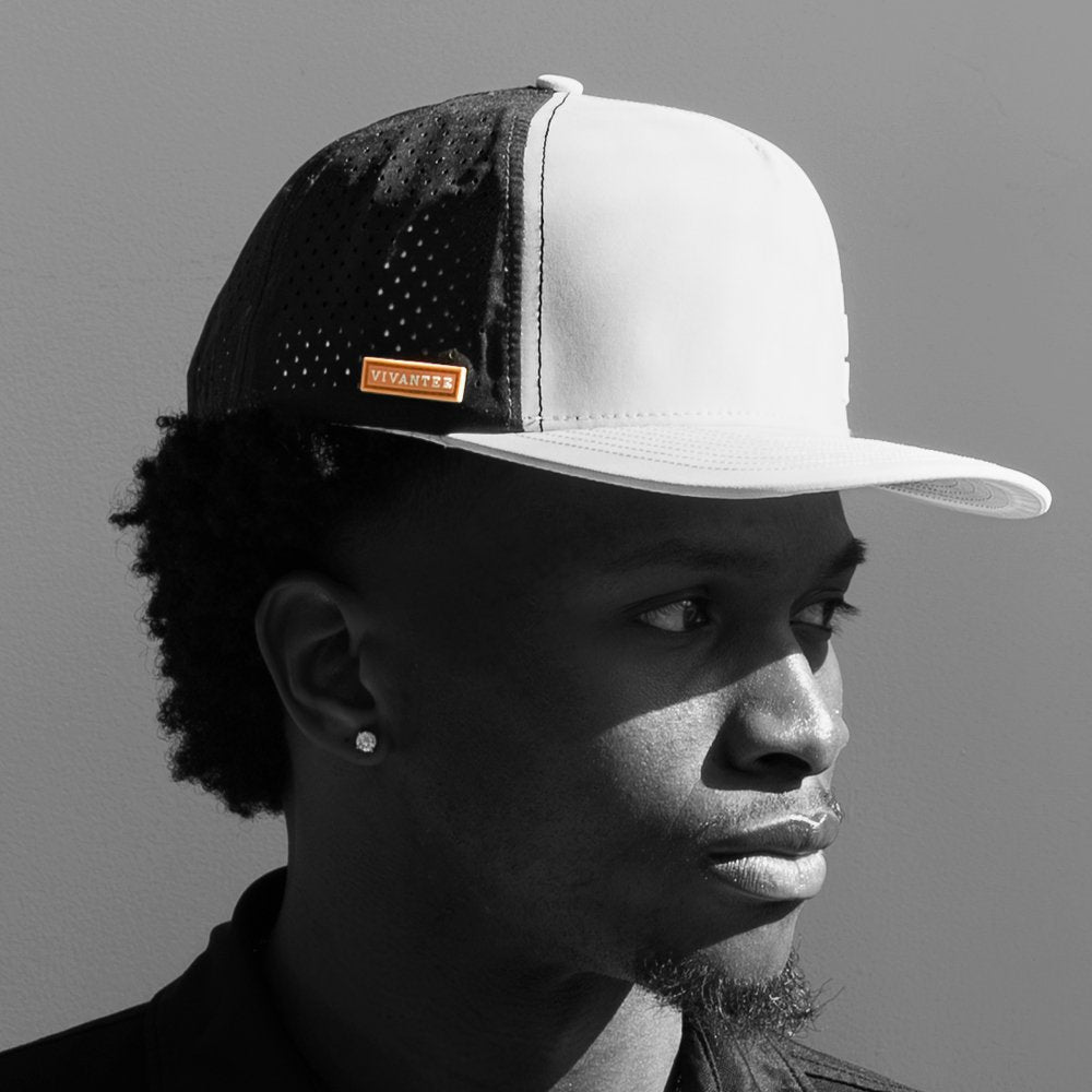 Model wearing a performance golf hat in black and white with only the orange logo on the hat in color.