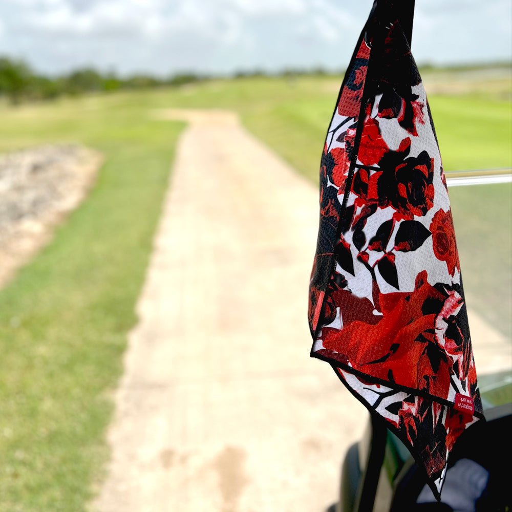 Red and black floral golf towel hanging from a golf cart on a golf course by VivanTee Golf.