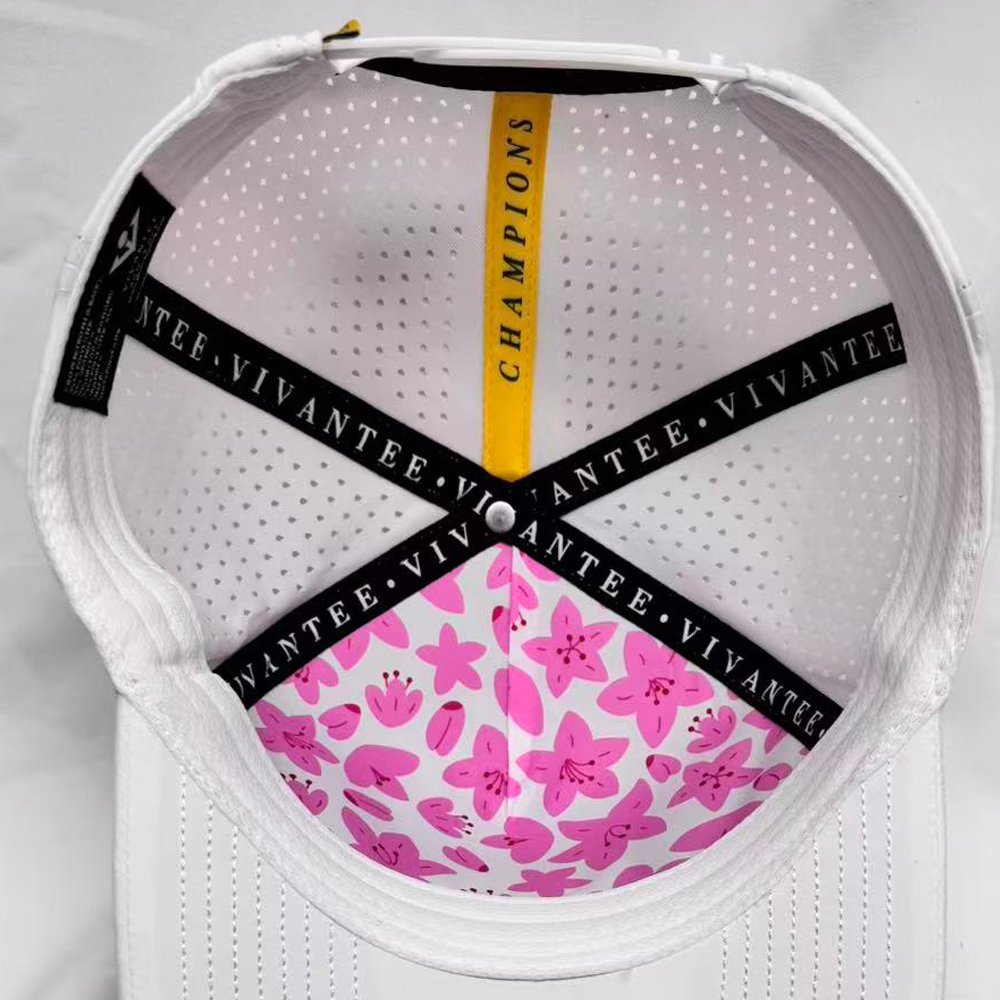 Close-up of a white golf hat with pink floral pattern and black text saying "VivanTee" on a light gray background