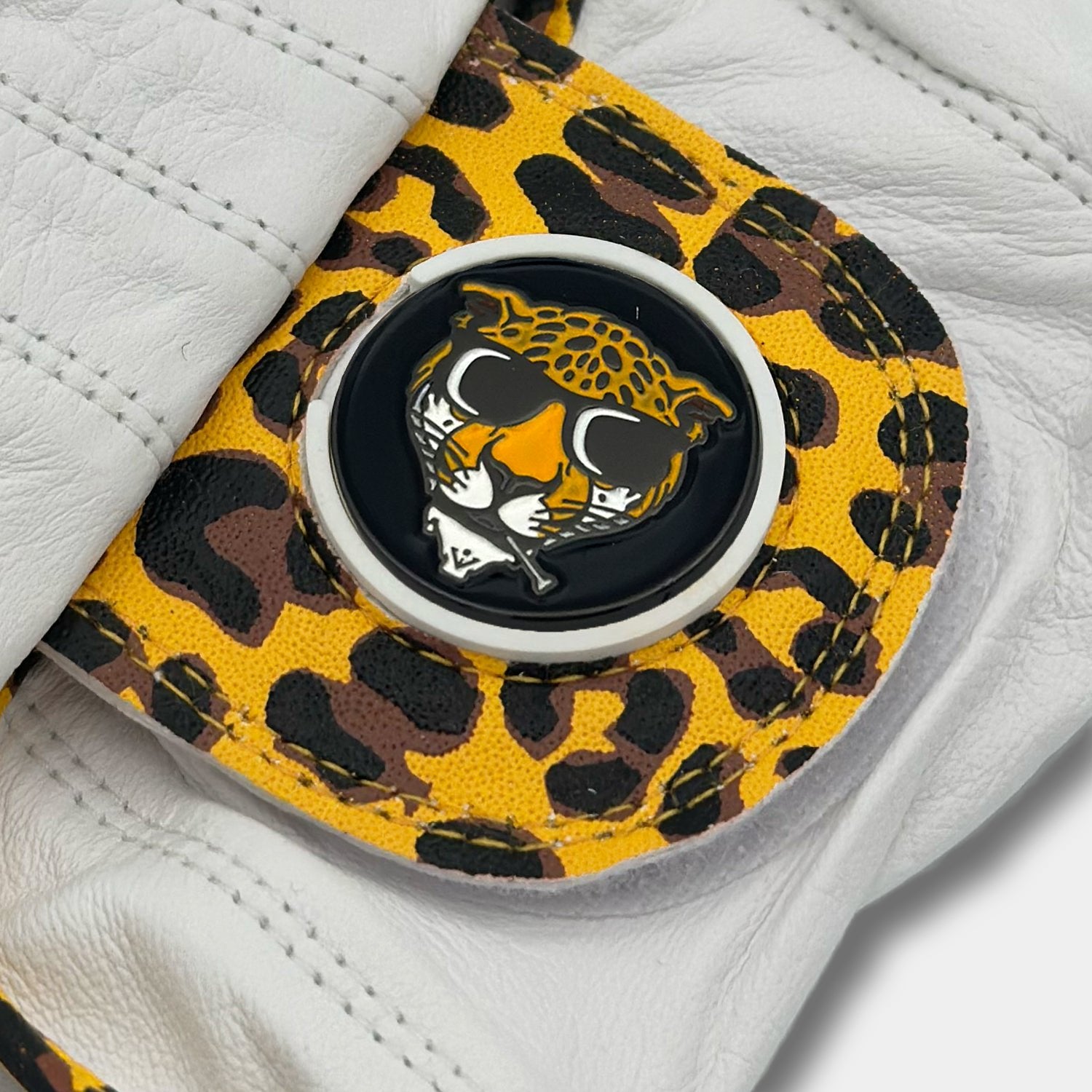 Close-up of a VivanTee Cabretta leather golf glove with a yellow leopard print design and the "cool cat" magnetic ball marker, blending style and performance.