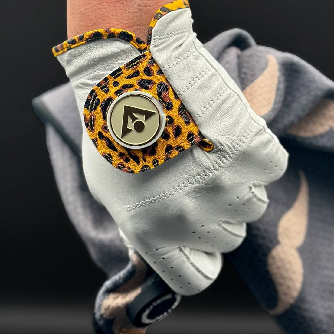 Cheetah print golf glove holding a magnetic golf towel by VivanTee Golf with a black background.