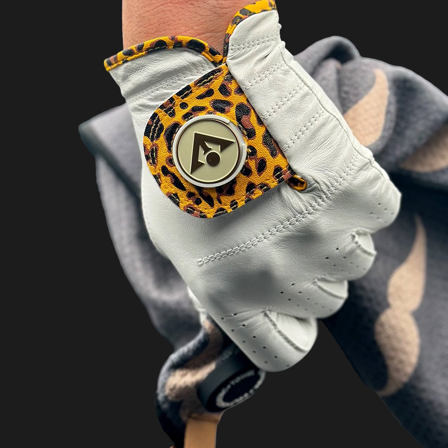 Image of a unique golf glove with ball marker in cheetah print close up and gripping a golf club.