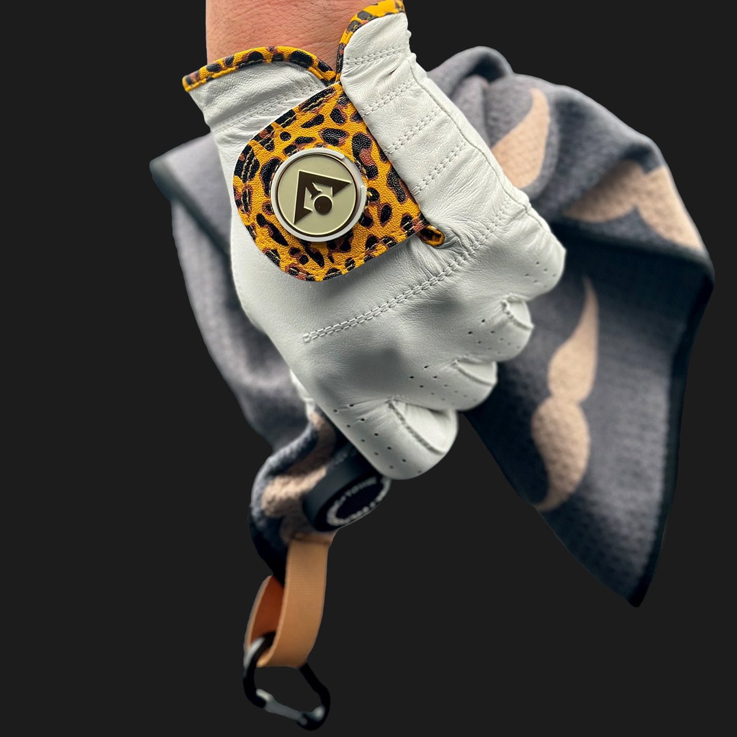 Image of a unique golf glove with ball marker in cheetah print close up and gripping a golf club.