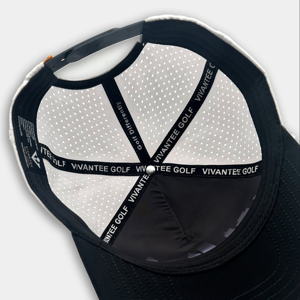 Modern snapback hat combining a black front section and bill with white perforated mesh panels. The front bears a matte black logo shaped like an abstract arrow and circle. The underside shows black fabric strips labeled “VIVANTEE GOLF.”