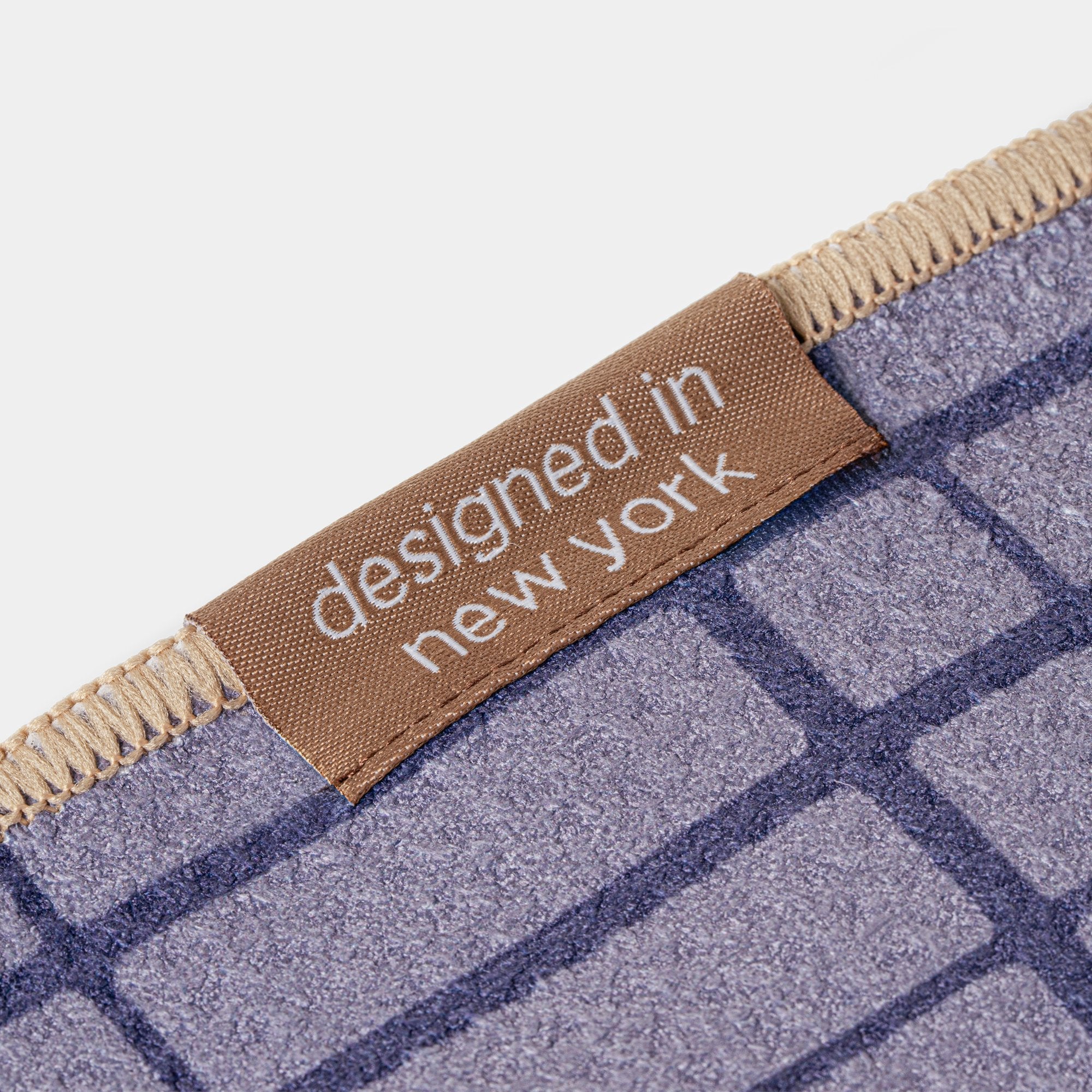 Golf towel in blue and brown with 'designed in New York' label on a checkered pattern background