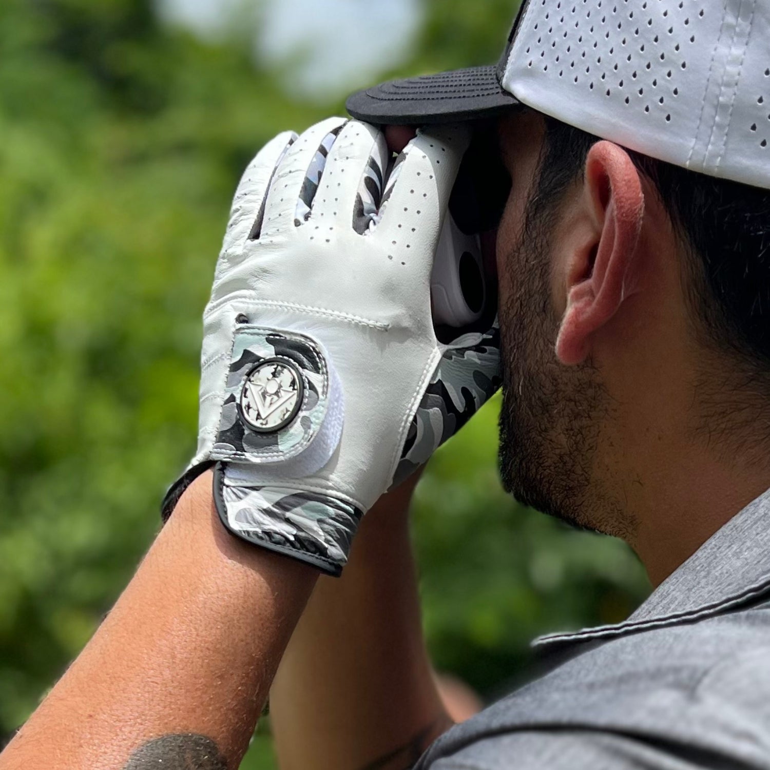 Person wearing a white golf glove and cap, looking through binoculars with a blurred green background