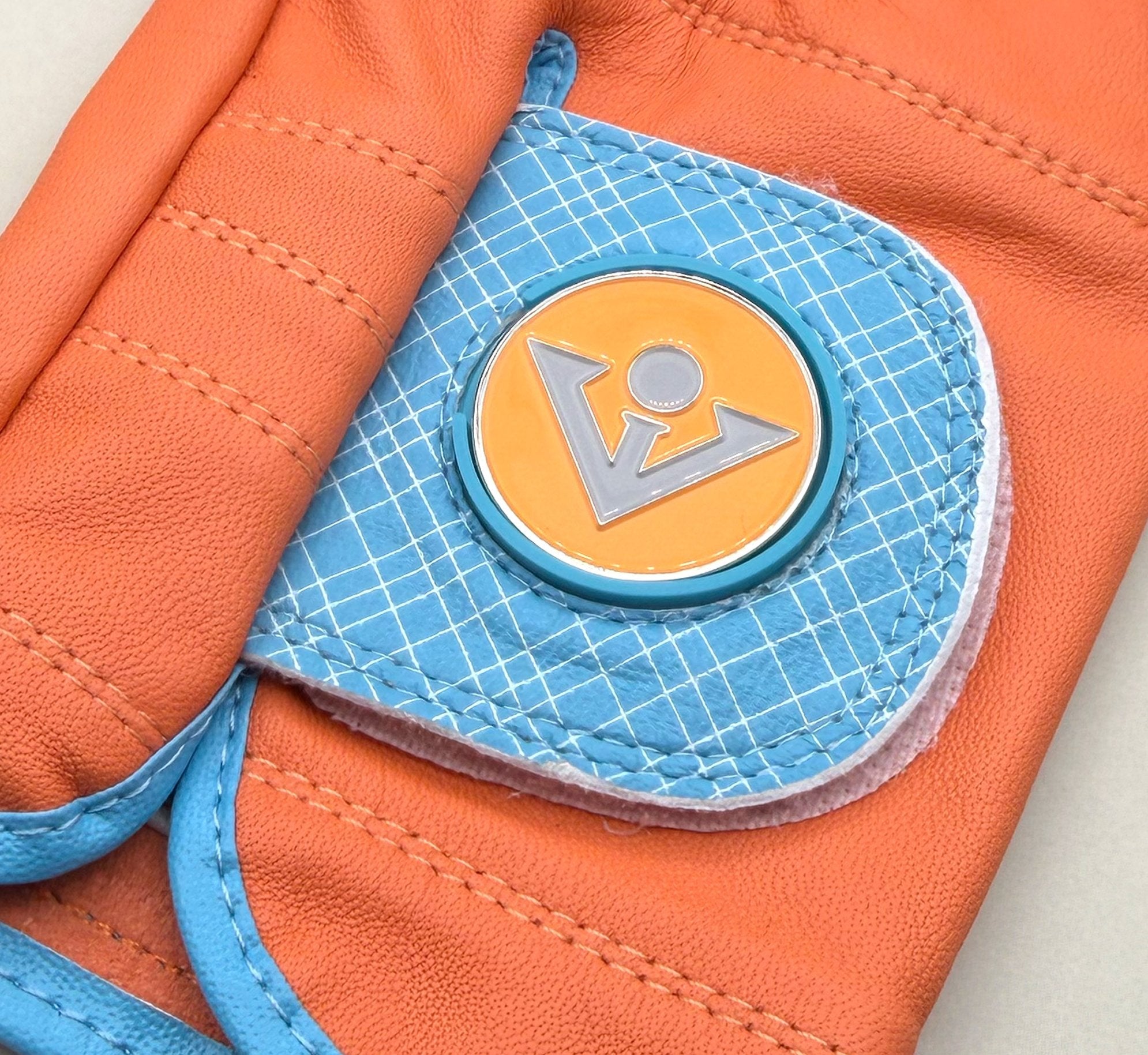 Close up of VivanTee orange golf glove with magnetic ball marker in blue on a white background.