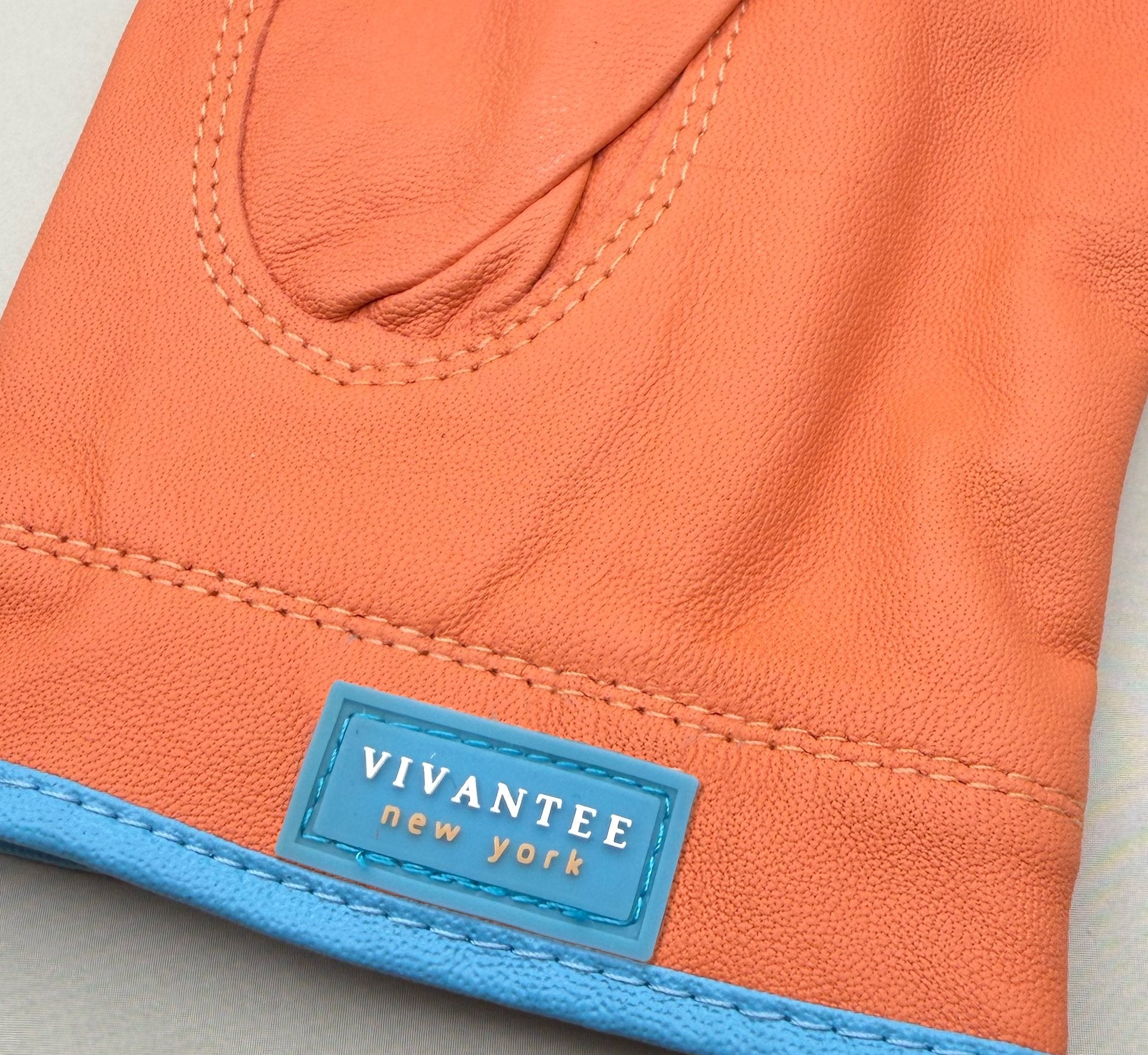 Close-up of orange leather golf glove with a blue label featuring 'Vivantee New York'.