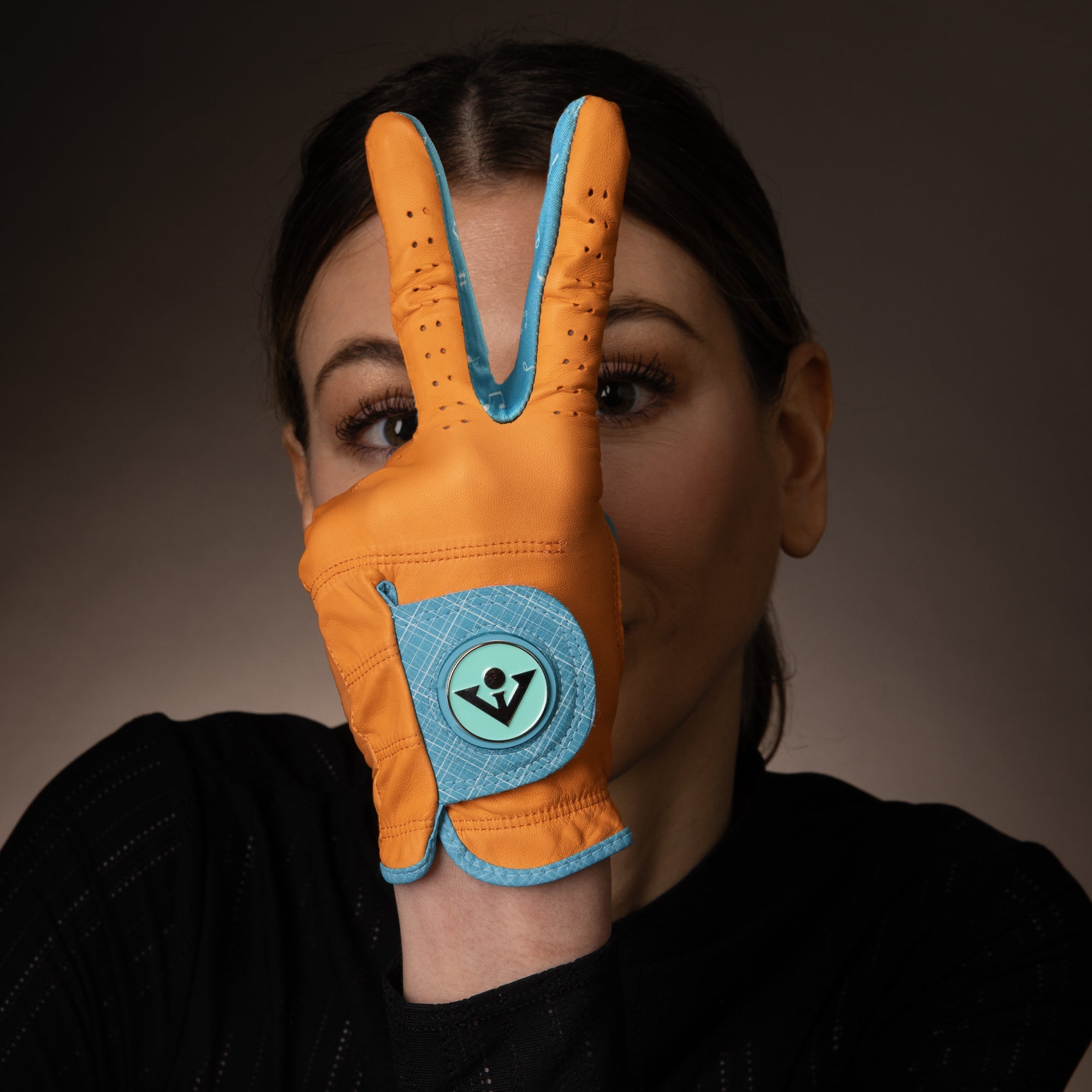 Woman in VivanTee orange golf glove holding up piece sign, showing the bright orange and blue accents.