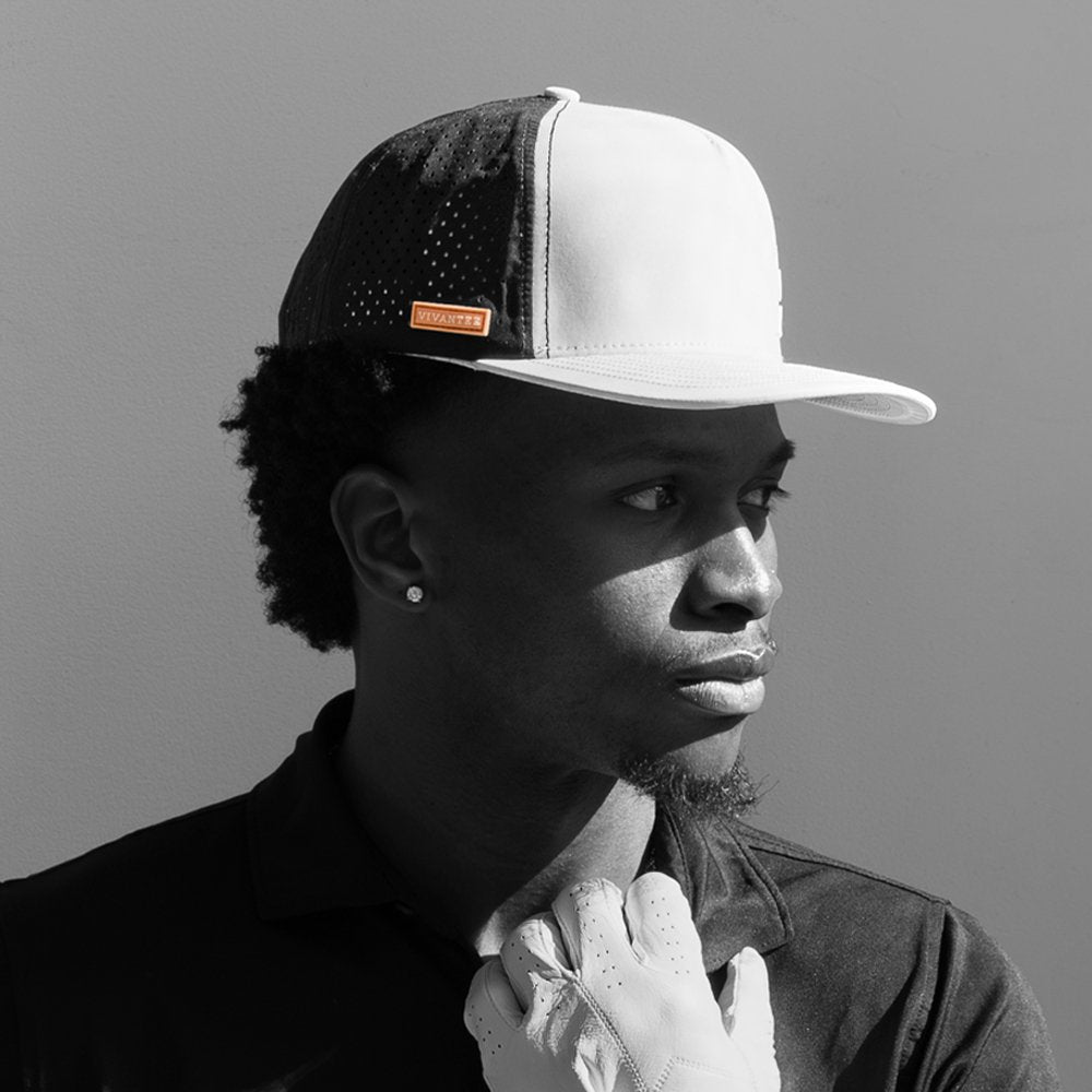Model wearing a performance golf hat in black and white with only the orange logo on the hat in color.