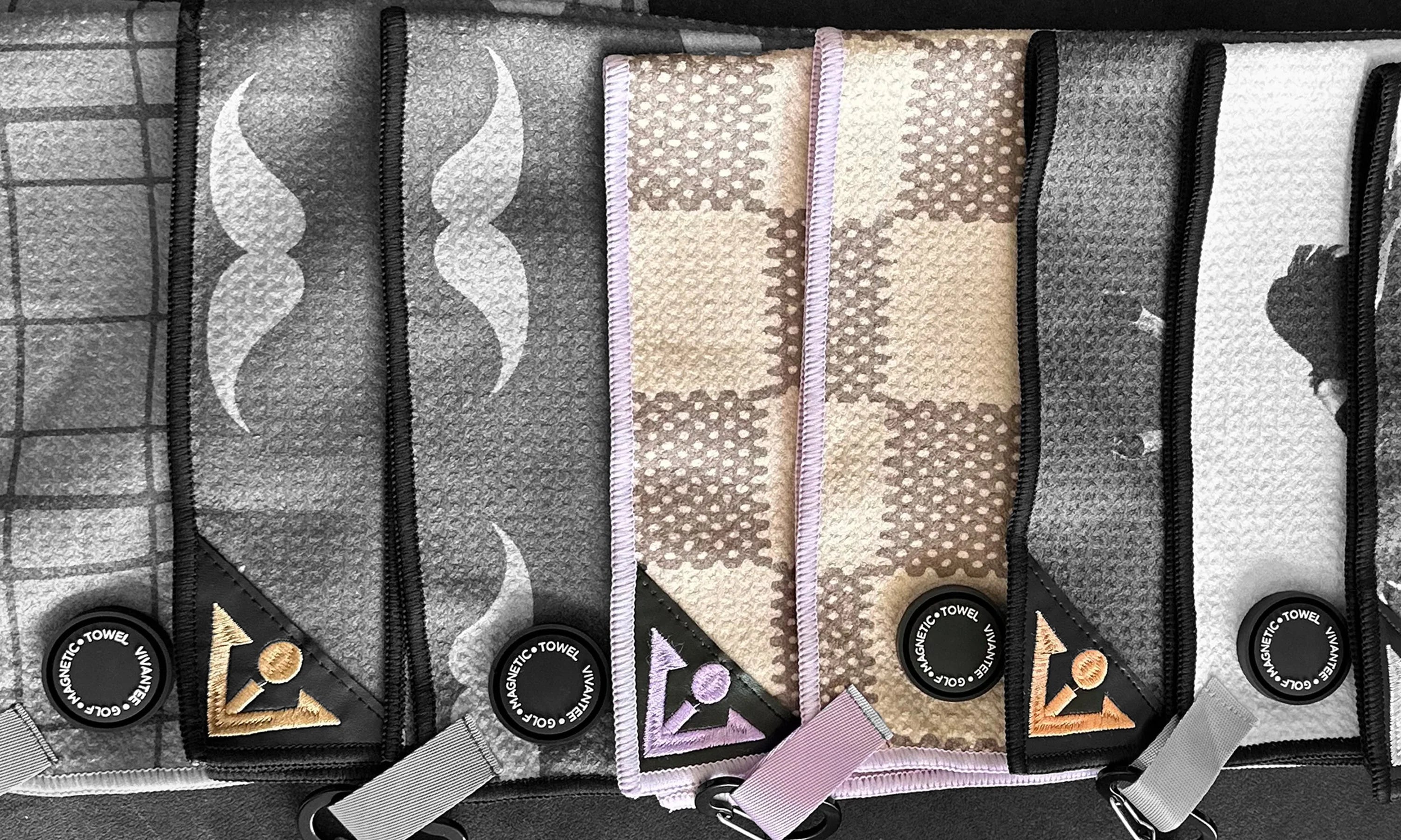 Various VivanTee Golf Magnetic golf towels lined up overlapping with only one in color, the rest in monochromatic.