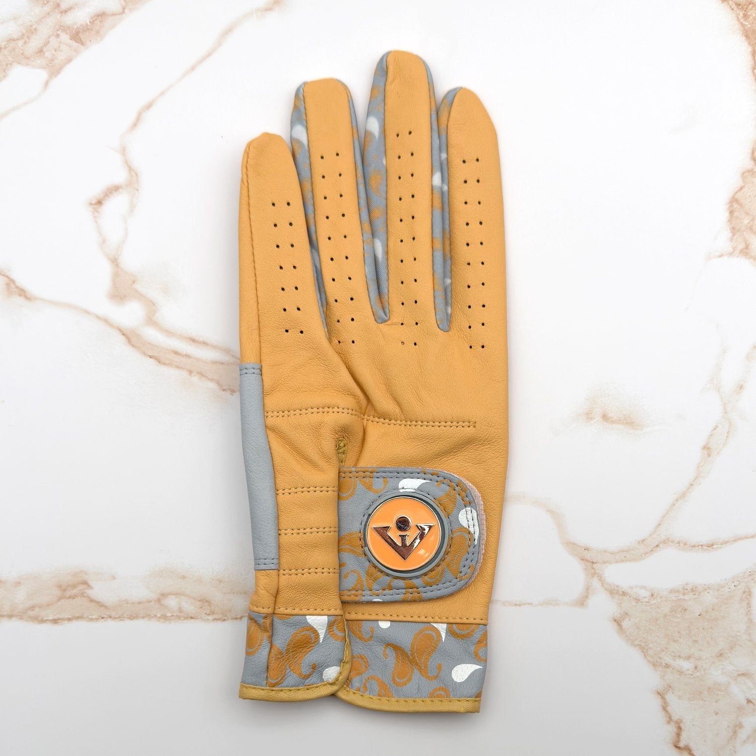 Gold and grey golf glove with paisley pattern laid out on granite counter top.