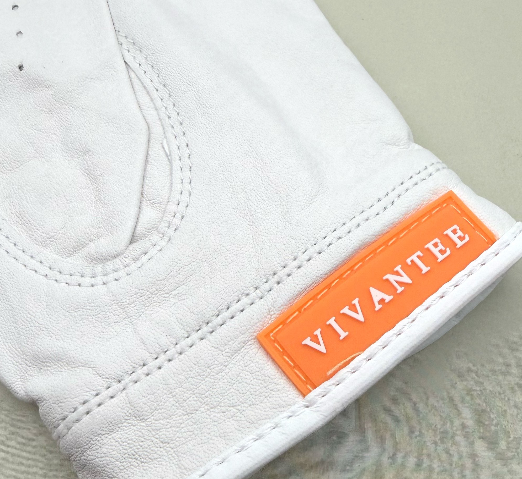 White golf glove with an orange 'Vivantee' label on a light gray background