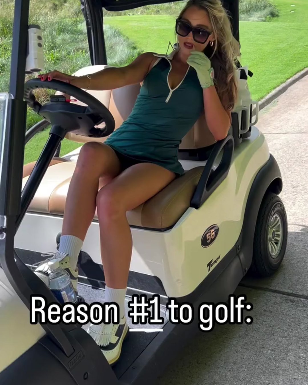 A fashionable woman lounging in a golf cart, wearing a dark green golf dress, oversized sunglasses, and a women's golf glove with a ball marker in a pastel green shade. The image conveys a relaxed, stylish golf lifestyle.