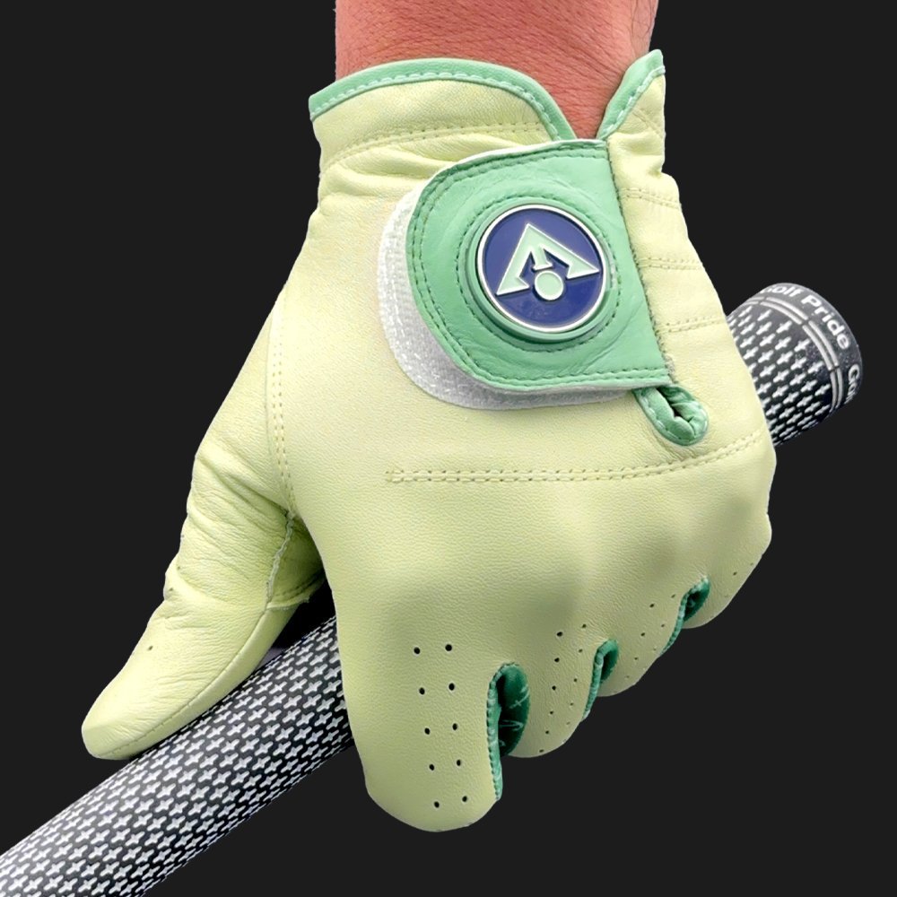 Close up of a light green golf glove with magnetic ball marker in blue by VivanTee Golf, holding a golf club with a dark background.