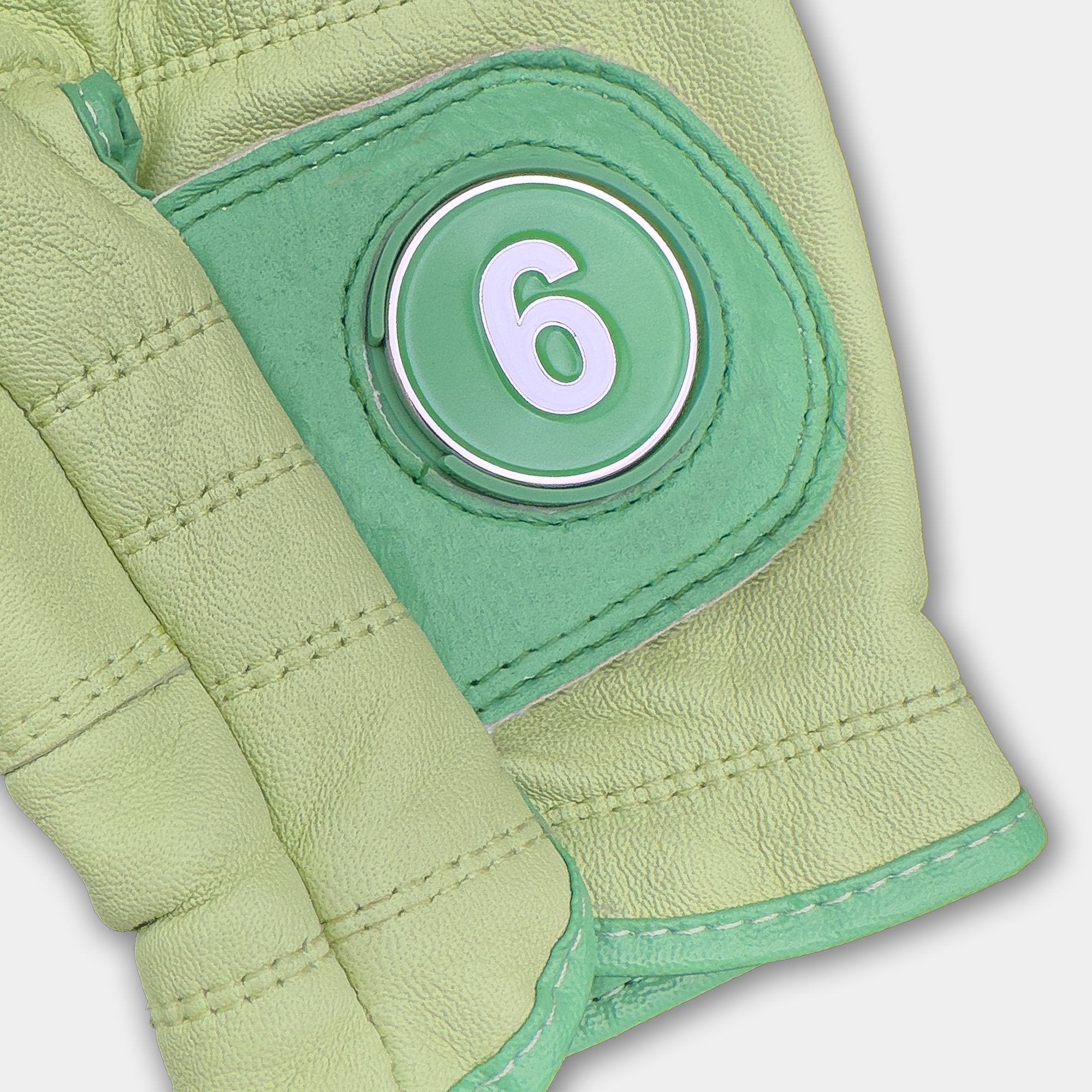 Green golf glove with a 6 train magnetic ball marker close up with grey background.
