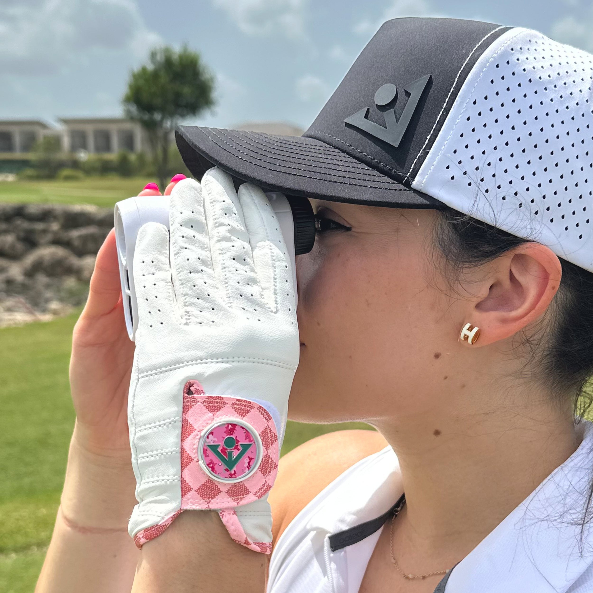 Women in a pink checkered golf glove by VivanTee Golf using a range finder up close.