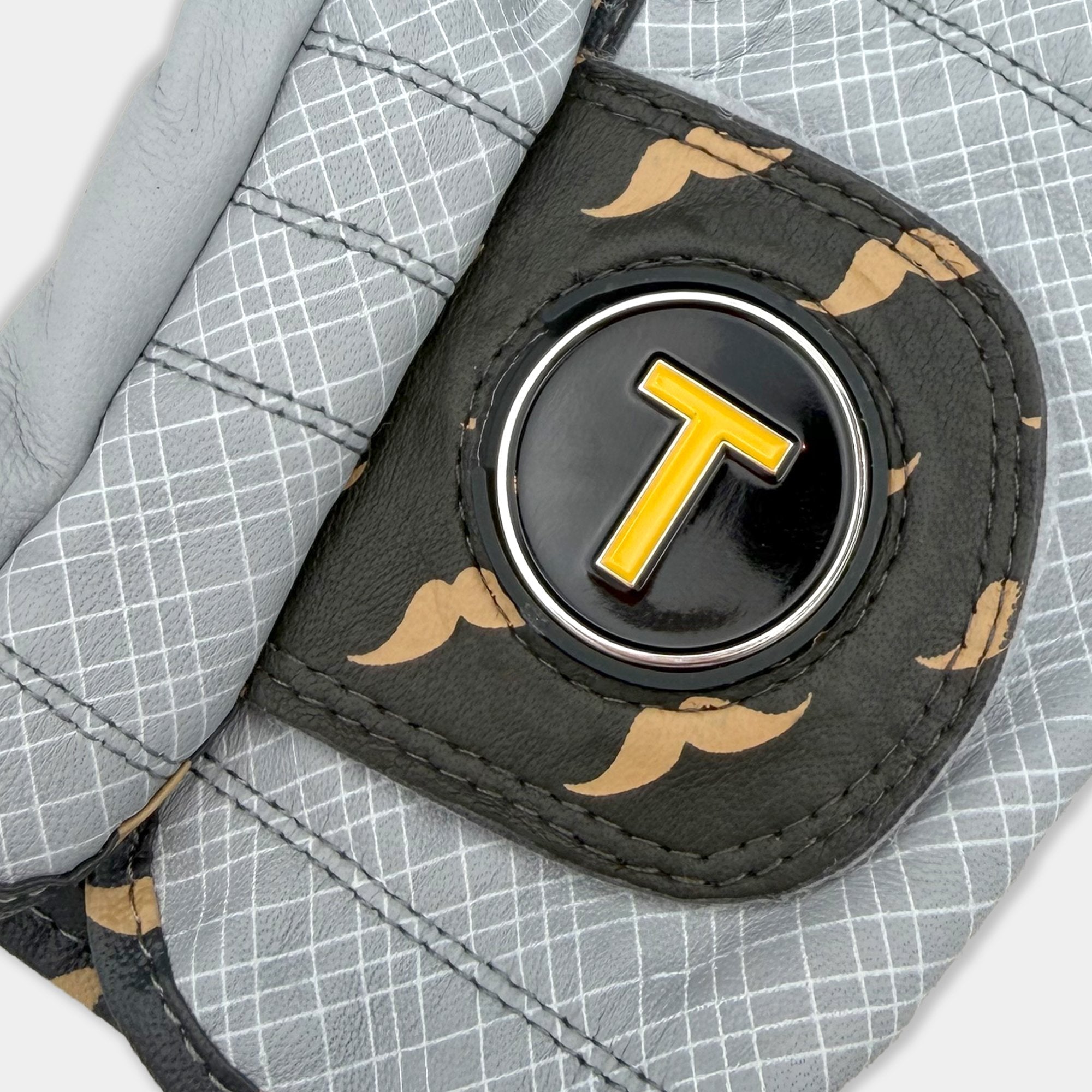 Close up of golf glove pull tag with orange magnetic ball marker with a stylish mustache pattern.