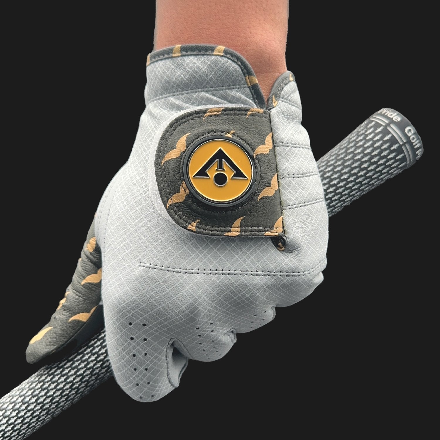 Gray golf glove with a logo on the back, holding a golf club against a black background