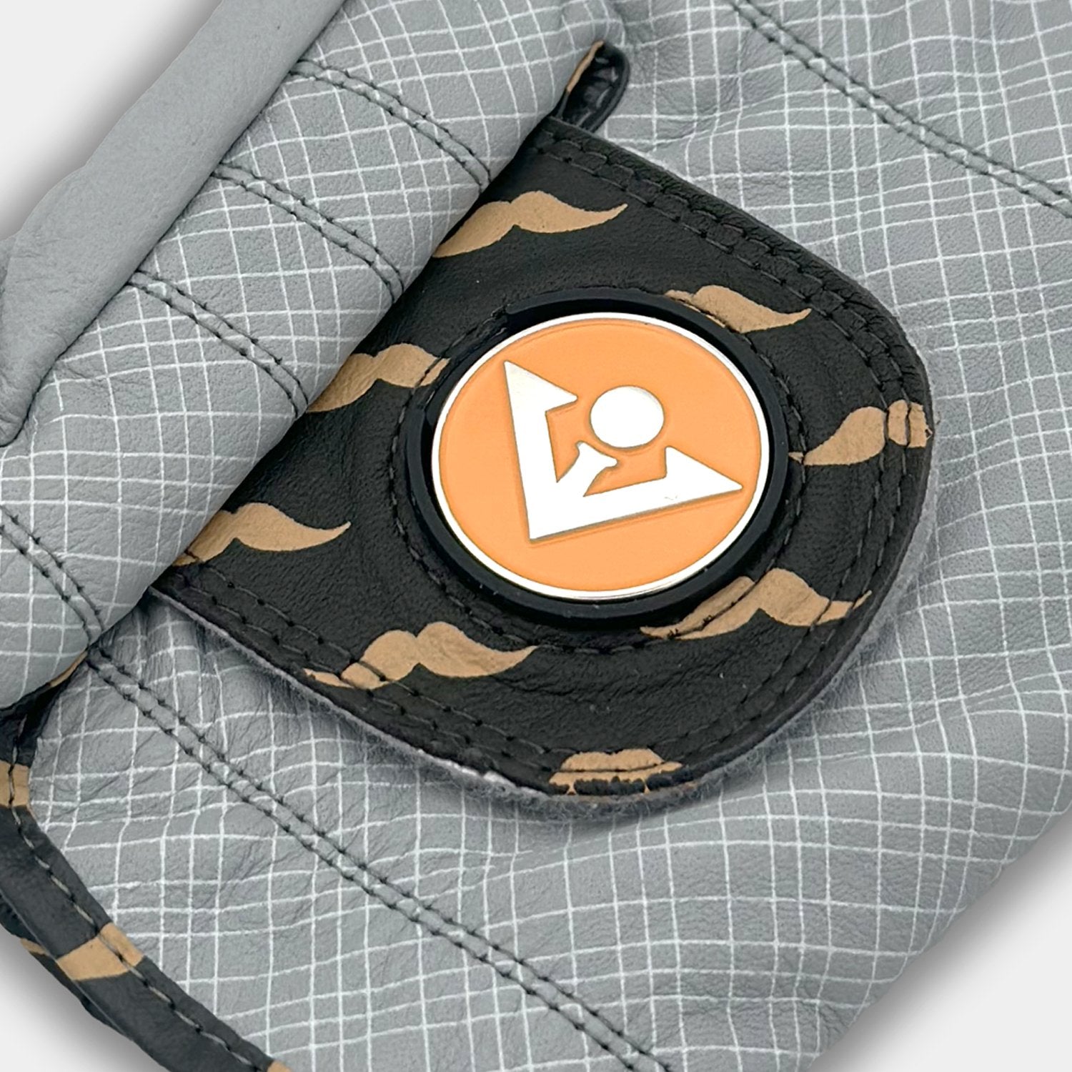 Close up of golf glove pull tag with orange magnetic ball marker with a stylish mustache pattern.