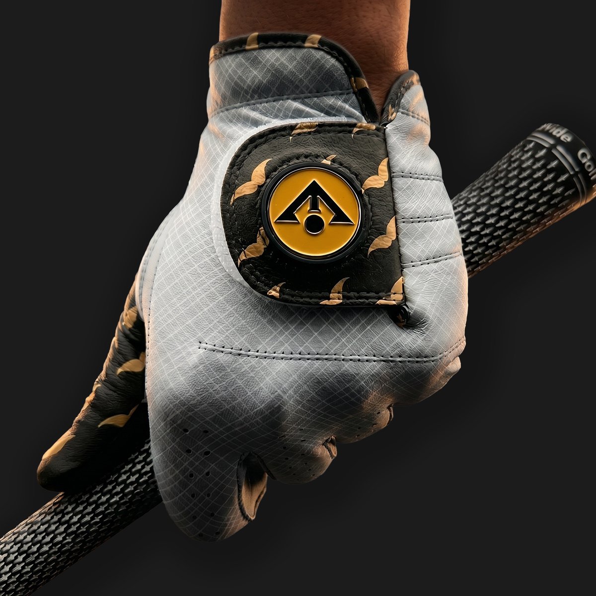 Gray golf glove with a logo on the back, holding a golf club against a black background