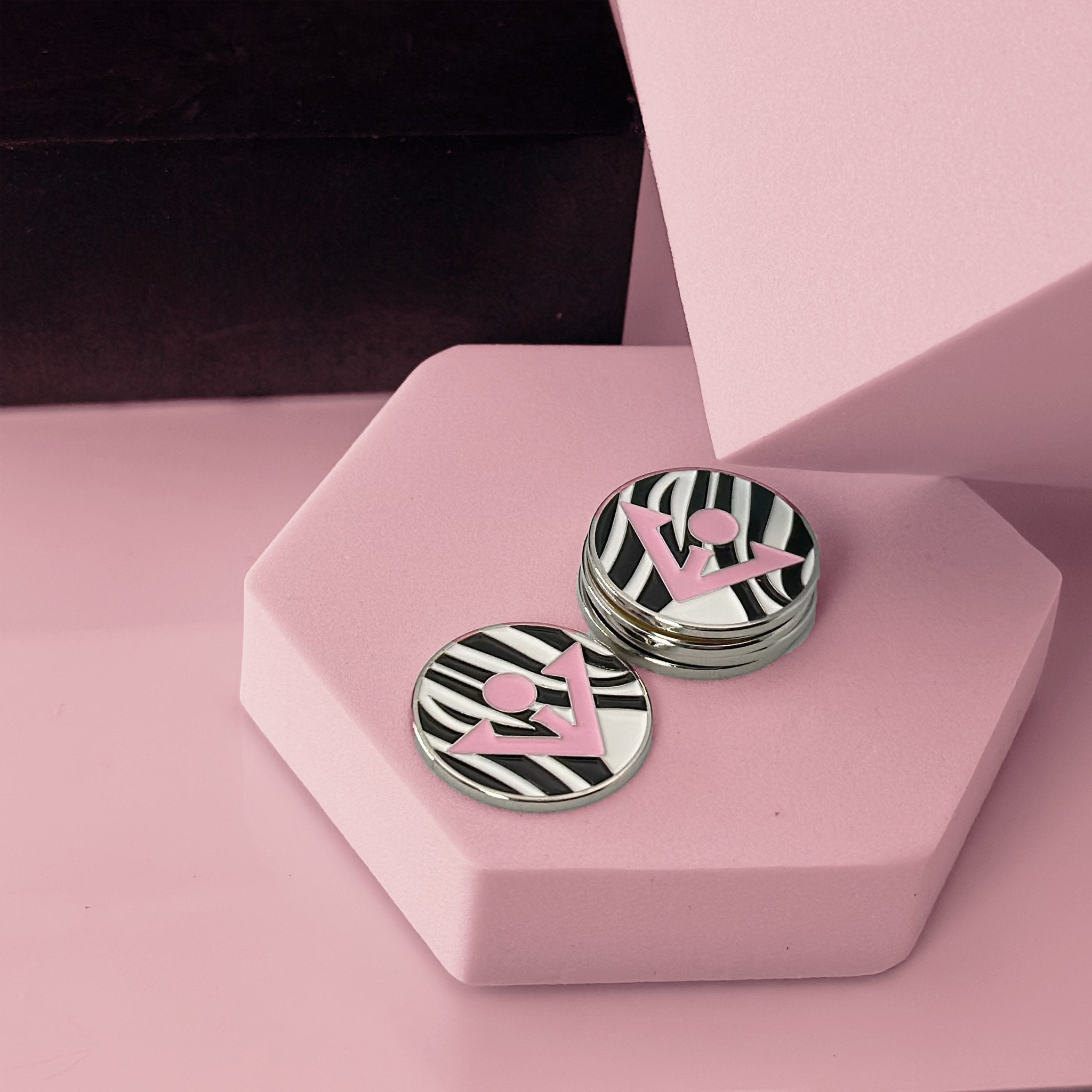 Zebra striped magnetic golf ball marker with pink VivanTee logo, surrounded by safari theme photoset.