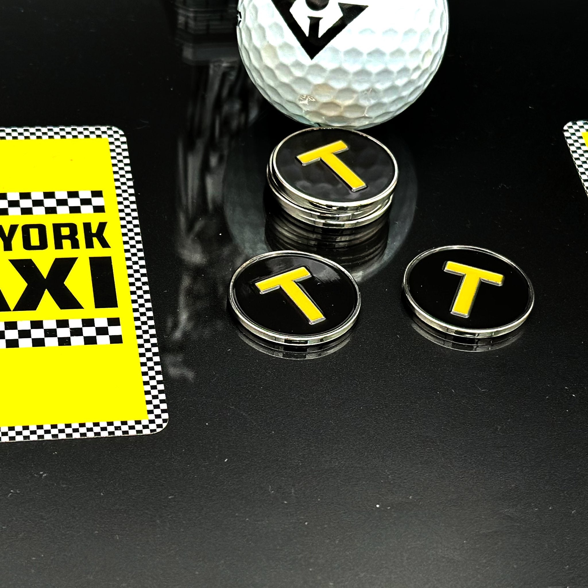 Magnetic Golf Ball Marker with the NYC Taxi Logo, next to a statue of liberty a NY Taxi checkered design.