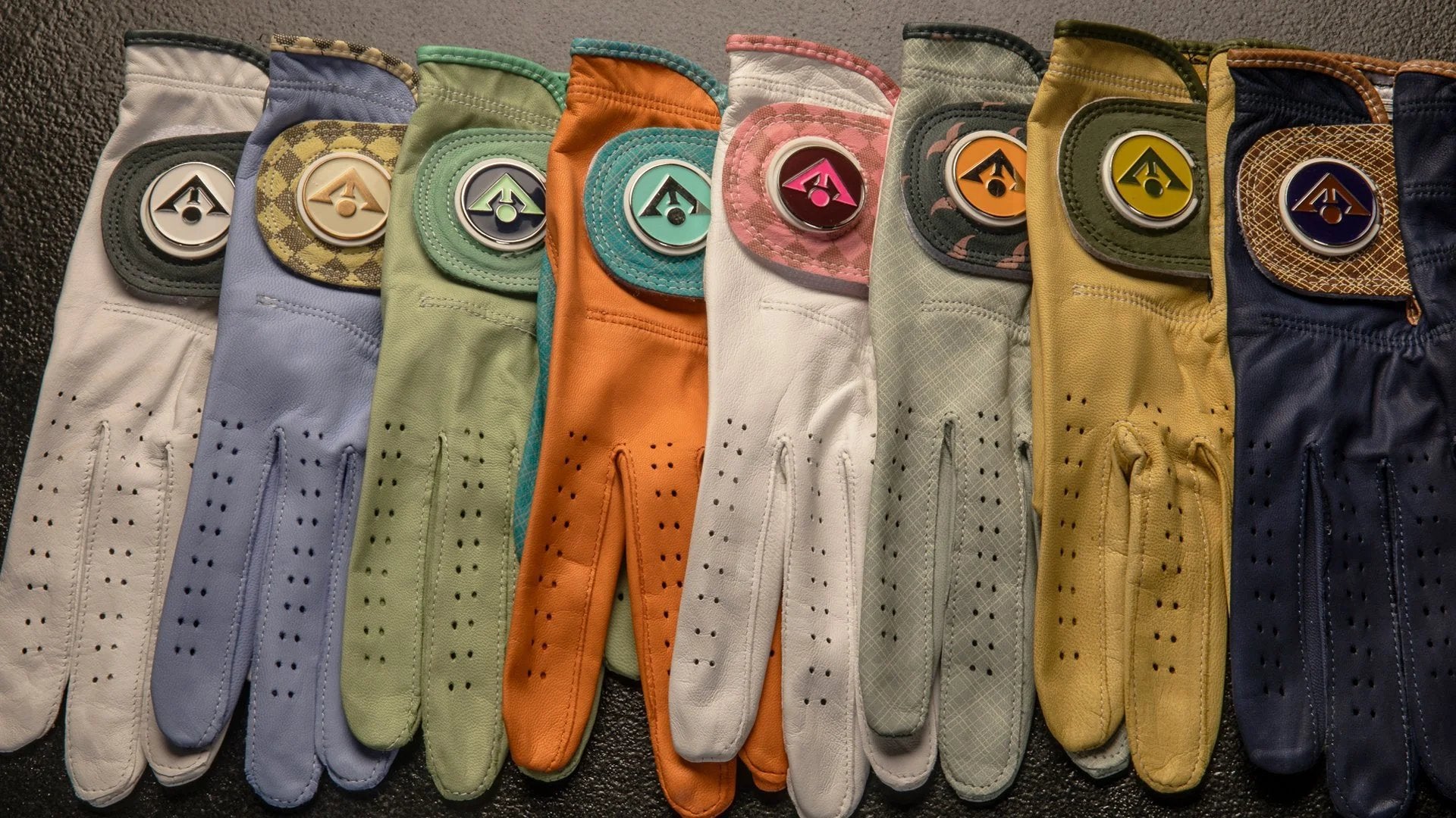 Designer golf gloves laid out in various colors show casing the vibrant hues of our designer golf gloves with markers.   with magnetic ball marker, glove in orange and blue.