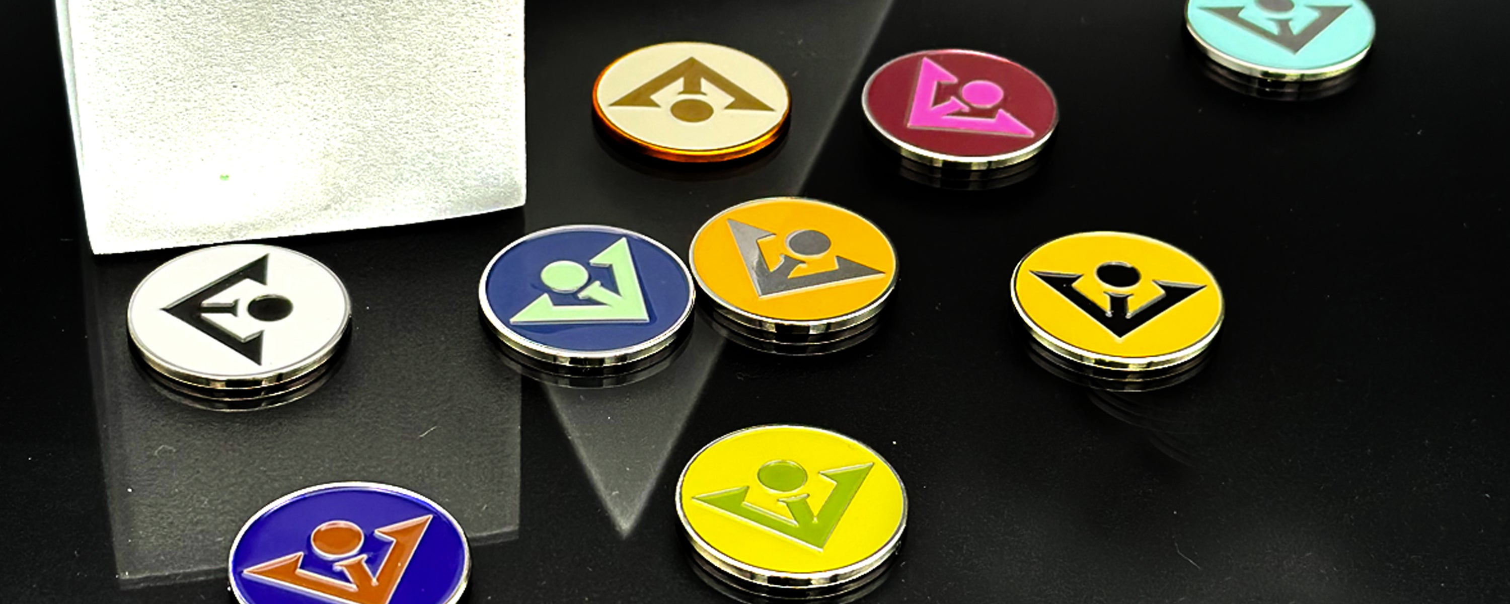 Various of our solid color ball markers with our logo on them scattered across a black and tile and white fixtures in the background, to compliment our magnetic golf gloves.