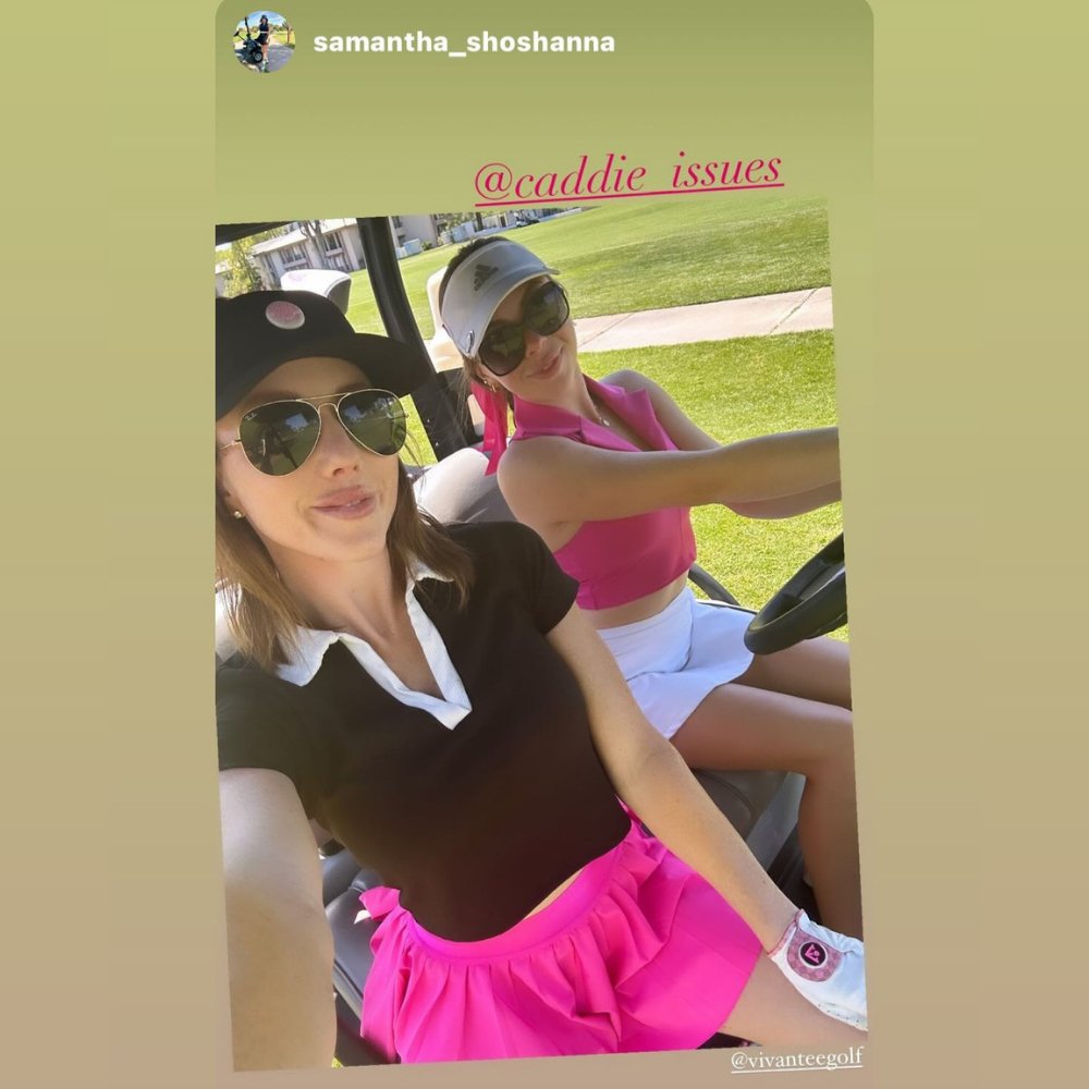 Two golfers in a cart, one wearing a unique white and pink golf glove with a magnetic ball marker, on a sunny golf course.