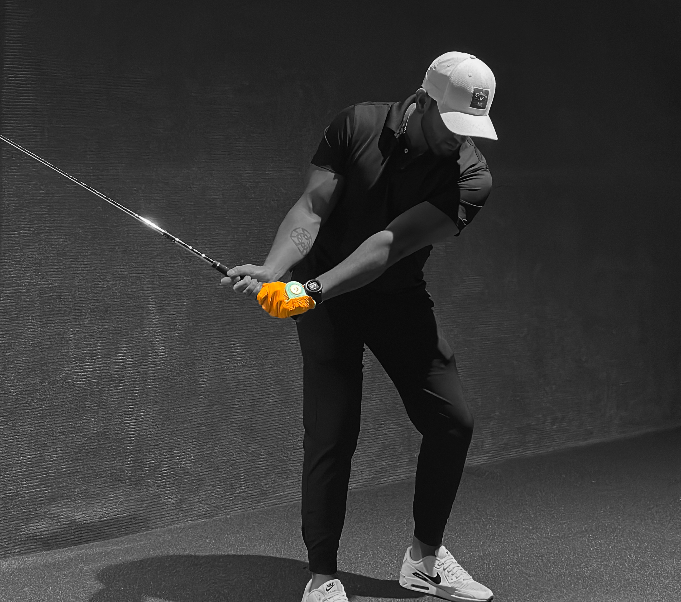 Founder of VivanTee golf gloves swinging golf club in simulator with an orange golf glove and black and white background. 