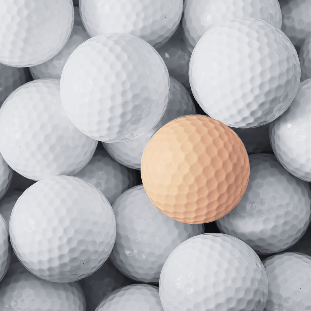 A group of golf balls in white with a single orange golf ball.