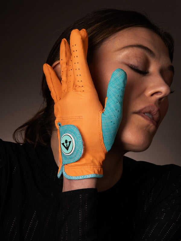 Woman posing with an orange golf glove and blue accents across her face and looking away.