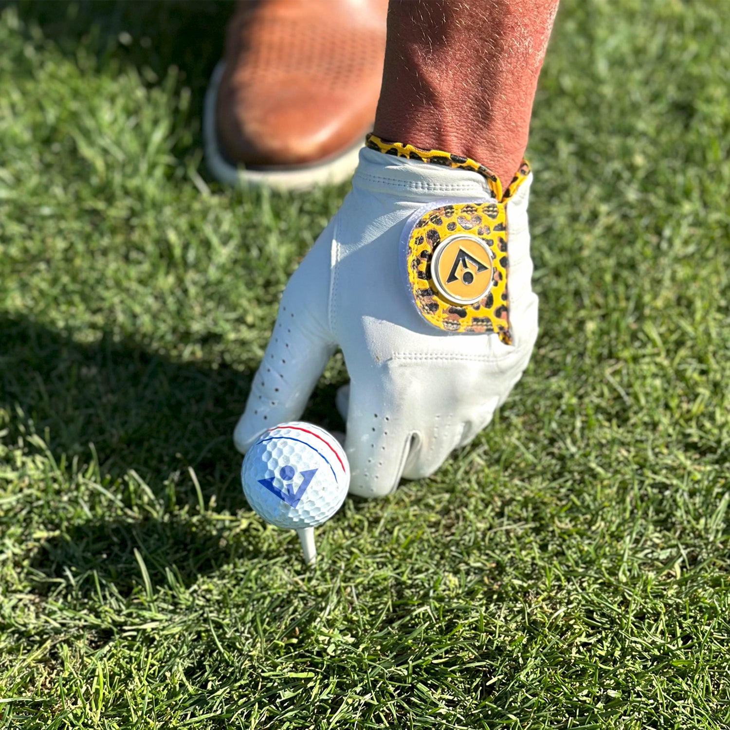Close up shot of a VivanTee golf glove in Cheetah print teeing up a golf ball with a VivanTee Logo.
