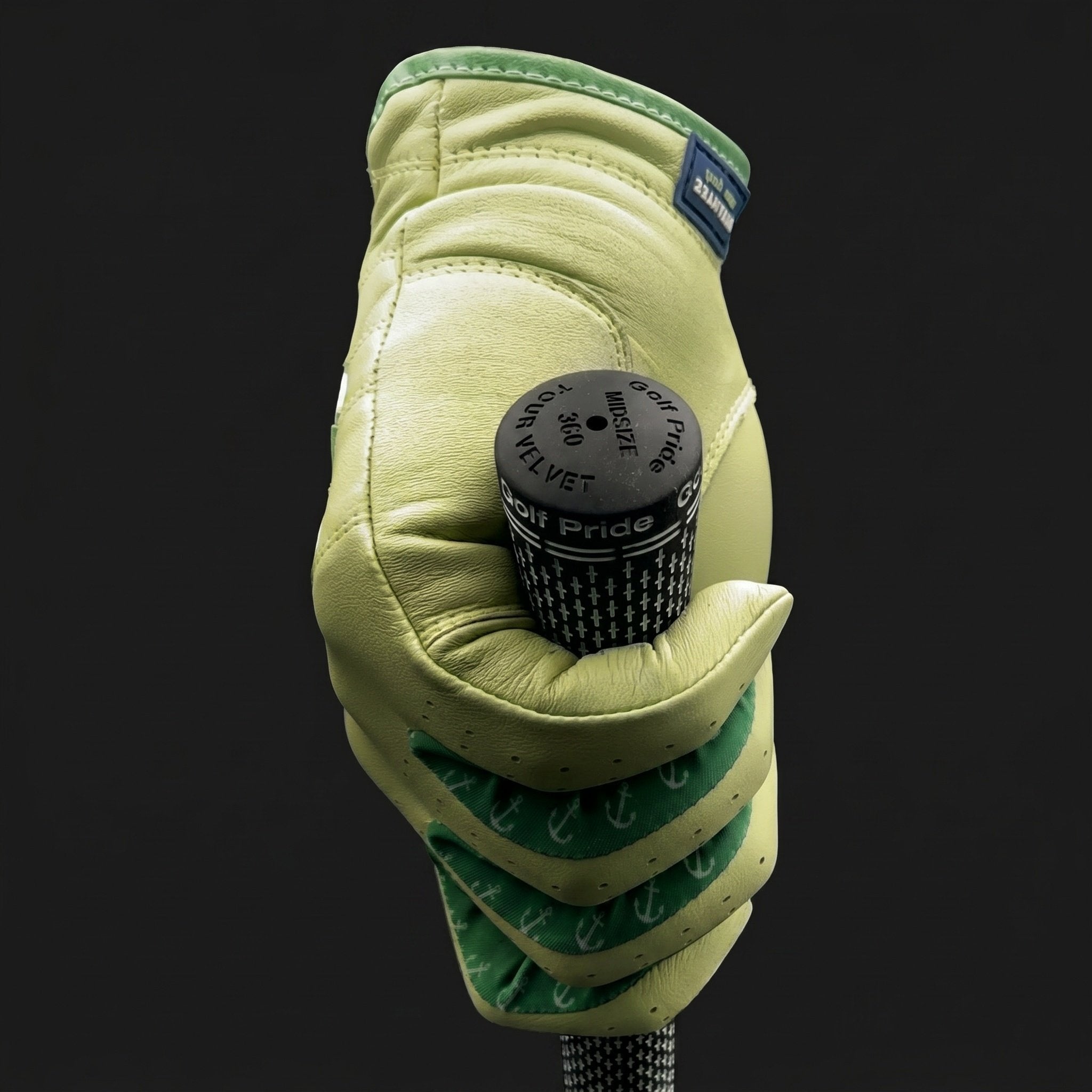 Hand wearing a green golf glove with lycra holding a golf club head cover against a black background.