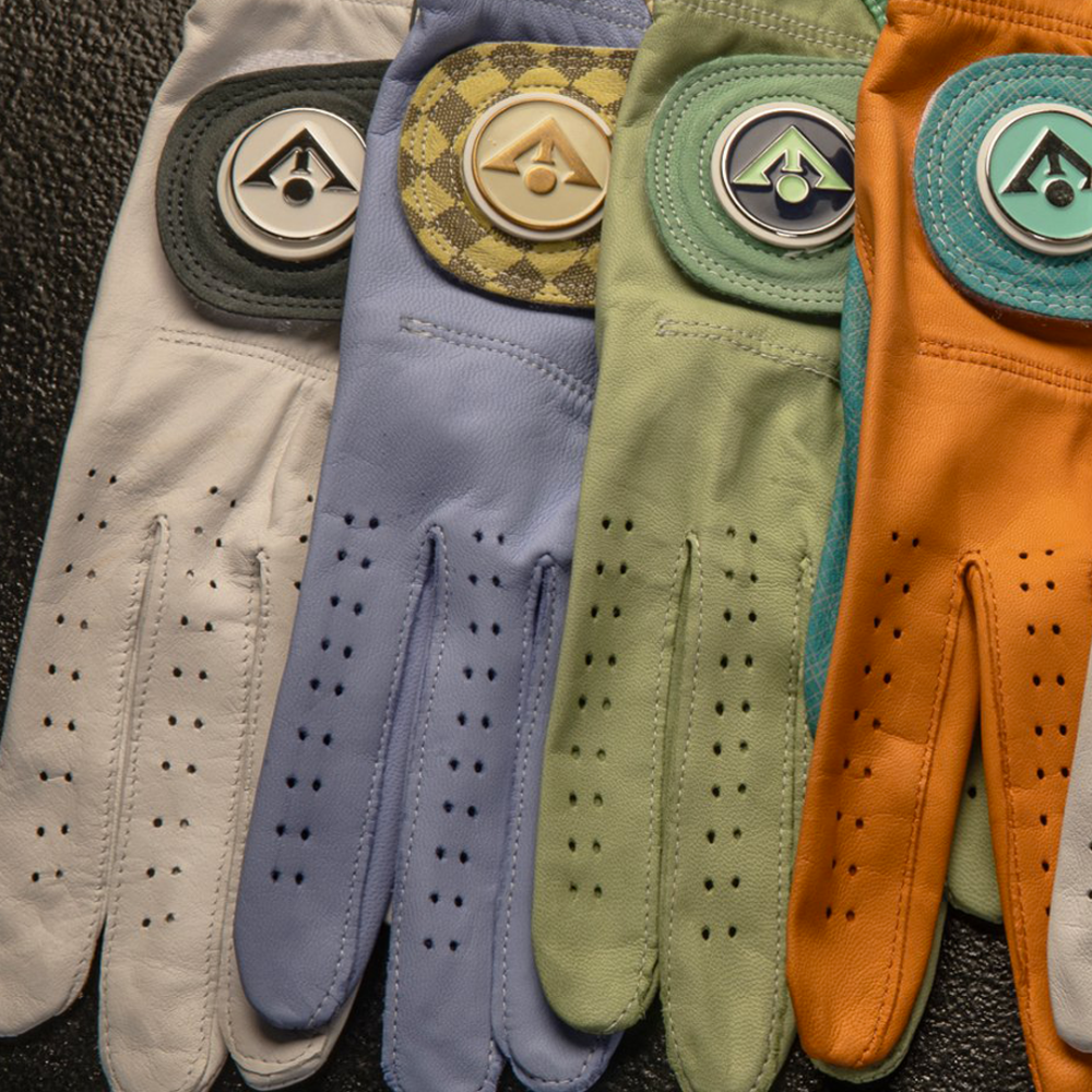 Multiple colored wholesale golf gloves in various hues and prints laid out overlapping one another with white, purple, green, and orange.  