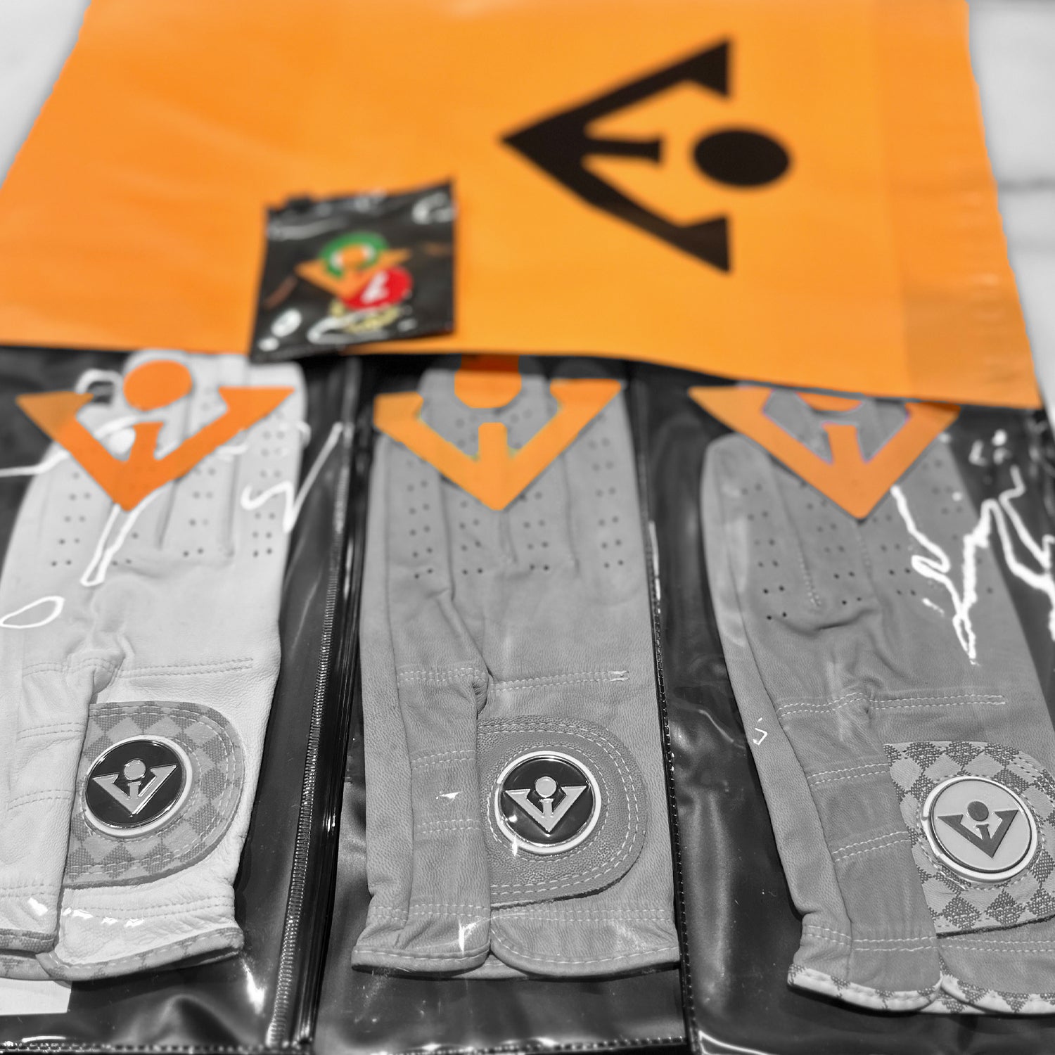 VivanTee golf gloves with ball markers in their packaging with the only colors in non black and white is the logo and our mailer back in orange.