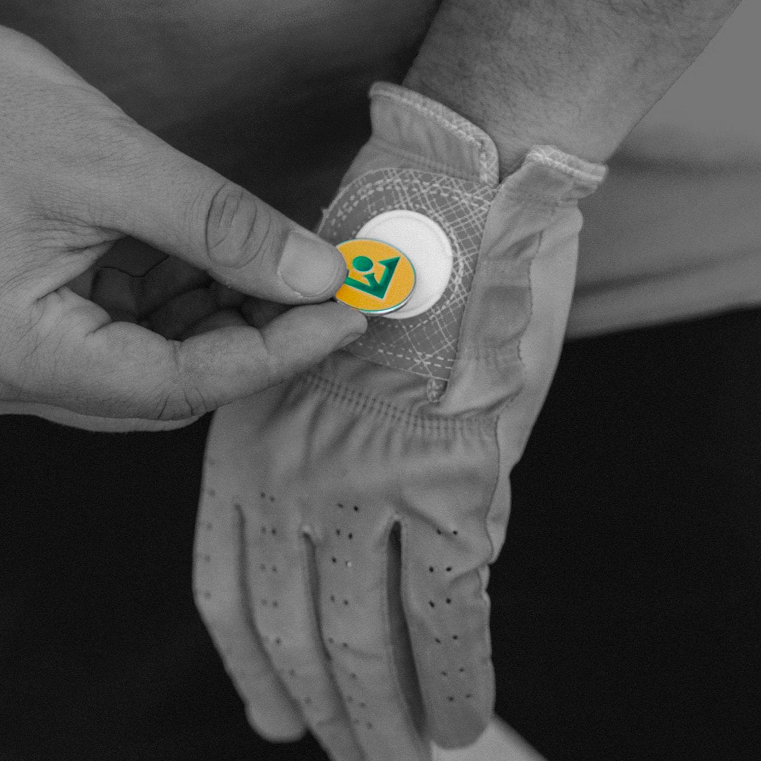 Golfer changing out magnetic ball marker on his glove in black and white, and the ball marker in orange color.  