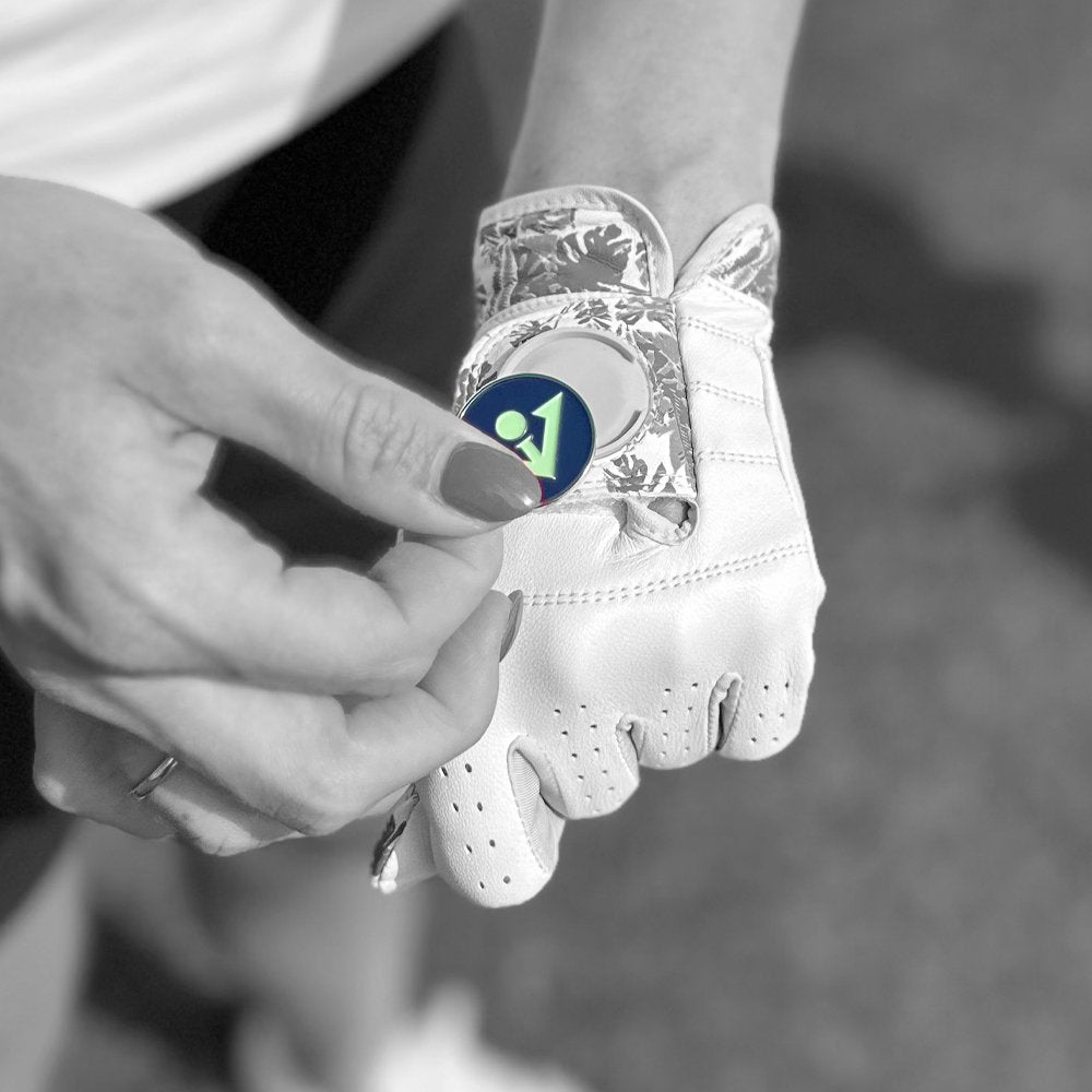 Close up of a VivanTee Golf glove with ball marker in black and white and woman putting a blue ball marker in place of the magnetic cavity.